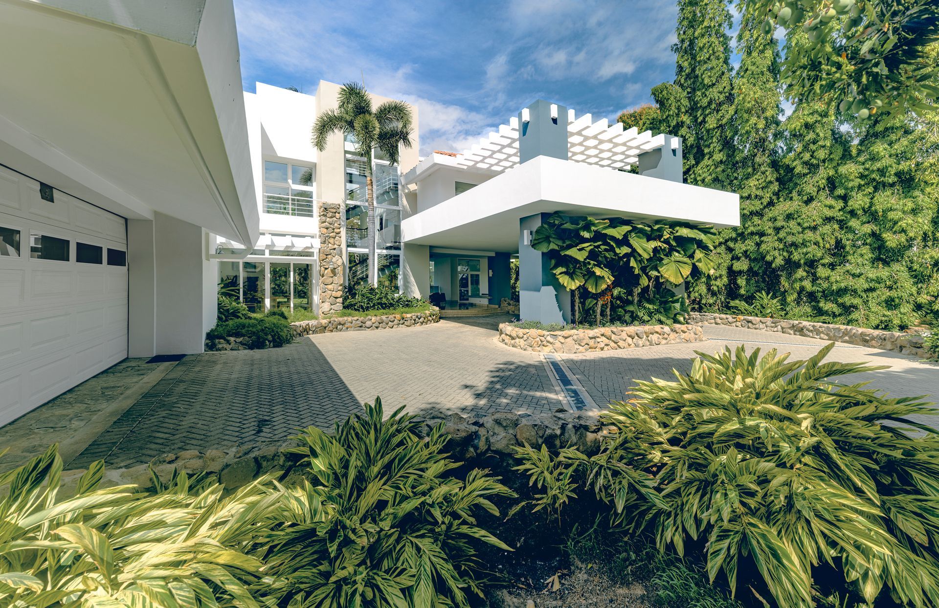 Luxury mansion entrance with manicured tropical gardens and modern white architecture in Punta Barco, Panama.