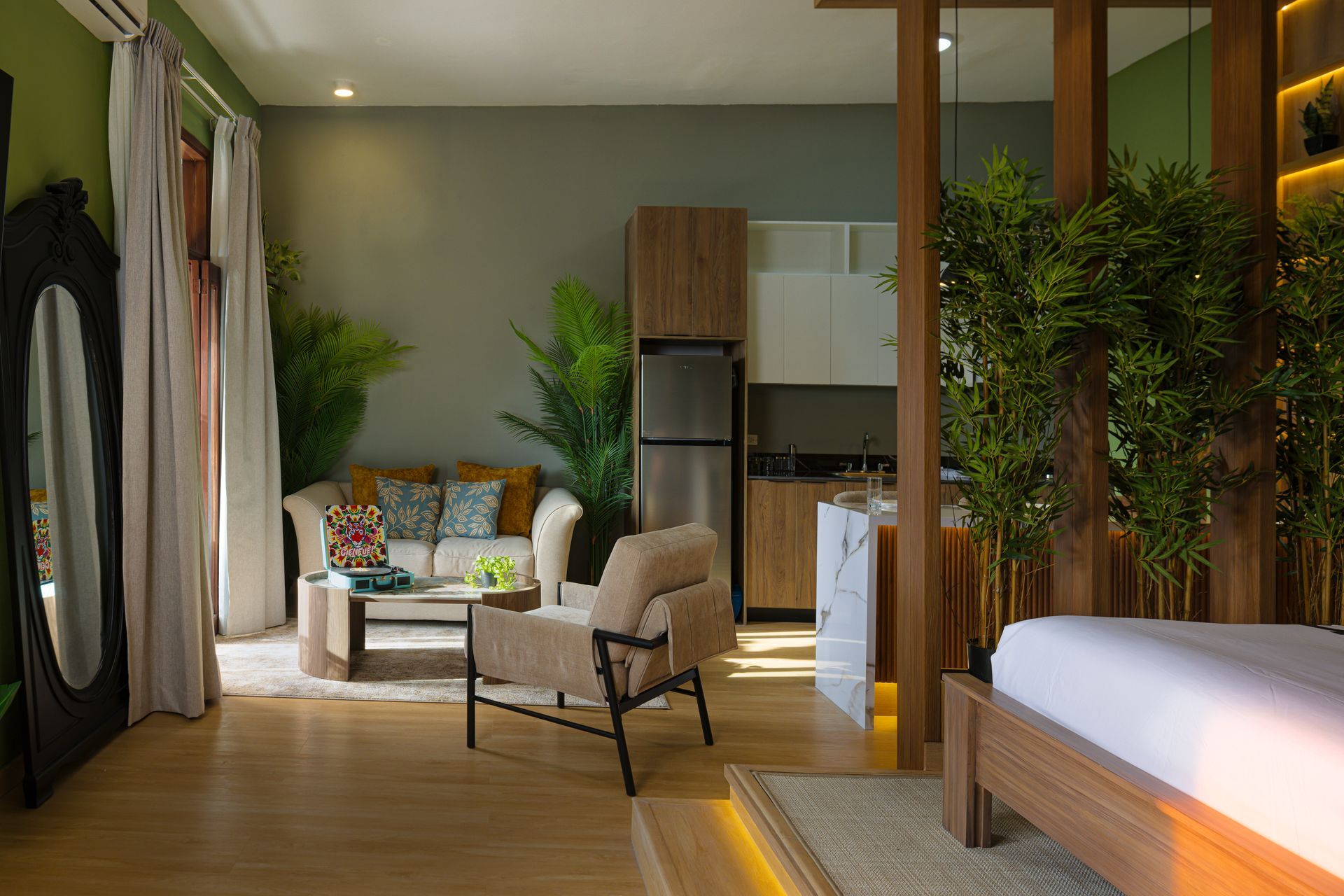 Studio interior at PH Hotel Colombia in Casco Viejo, featuring a wooden bed platform, leafy plants, beige lounge seating, and a compact kitchen.