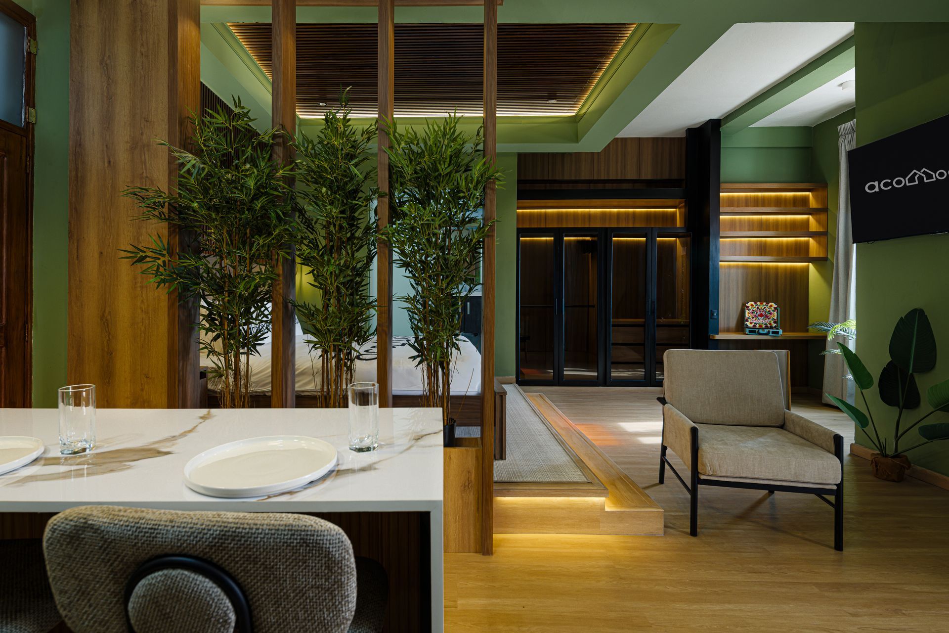 Interior at PH Hotel Colombia in Casco Viejo, featuring a dining table, plants between wooden dividers, a beige armchair, and illuminated steps leading to the sleeping area