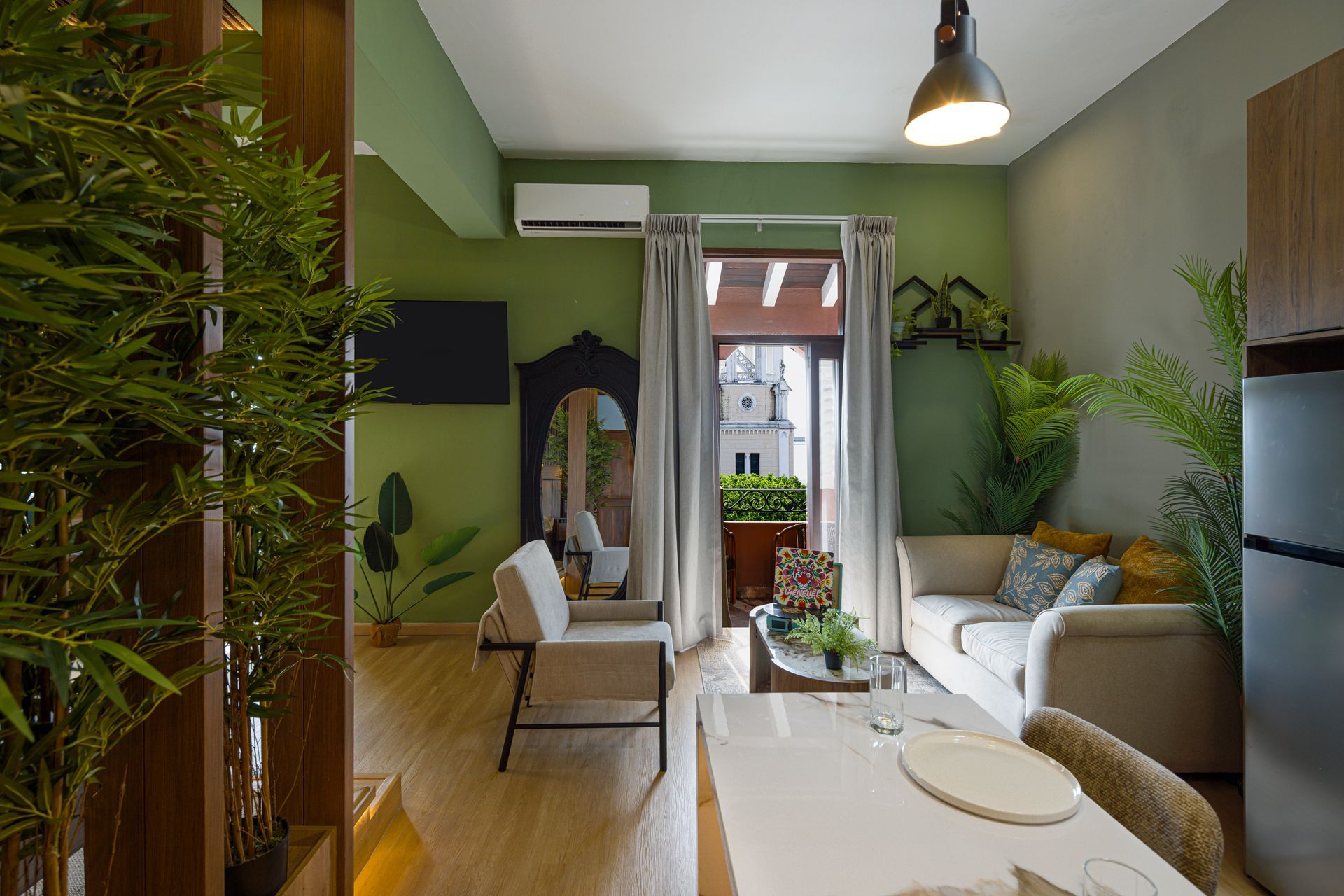 Lounge at PH Hotel Colombia with green walls, cream seating, tropical plants, and an open doorway framing San Francisco de Asís Church.