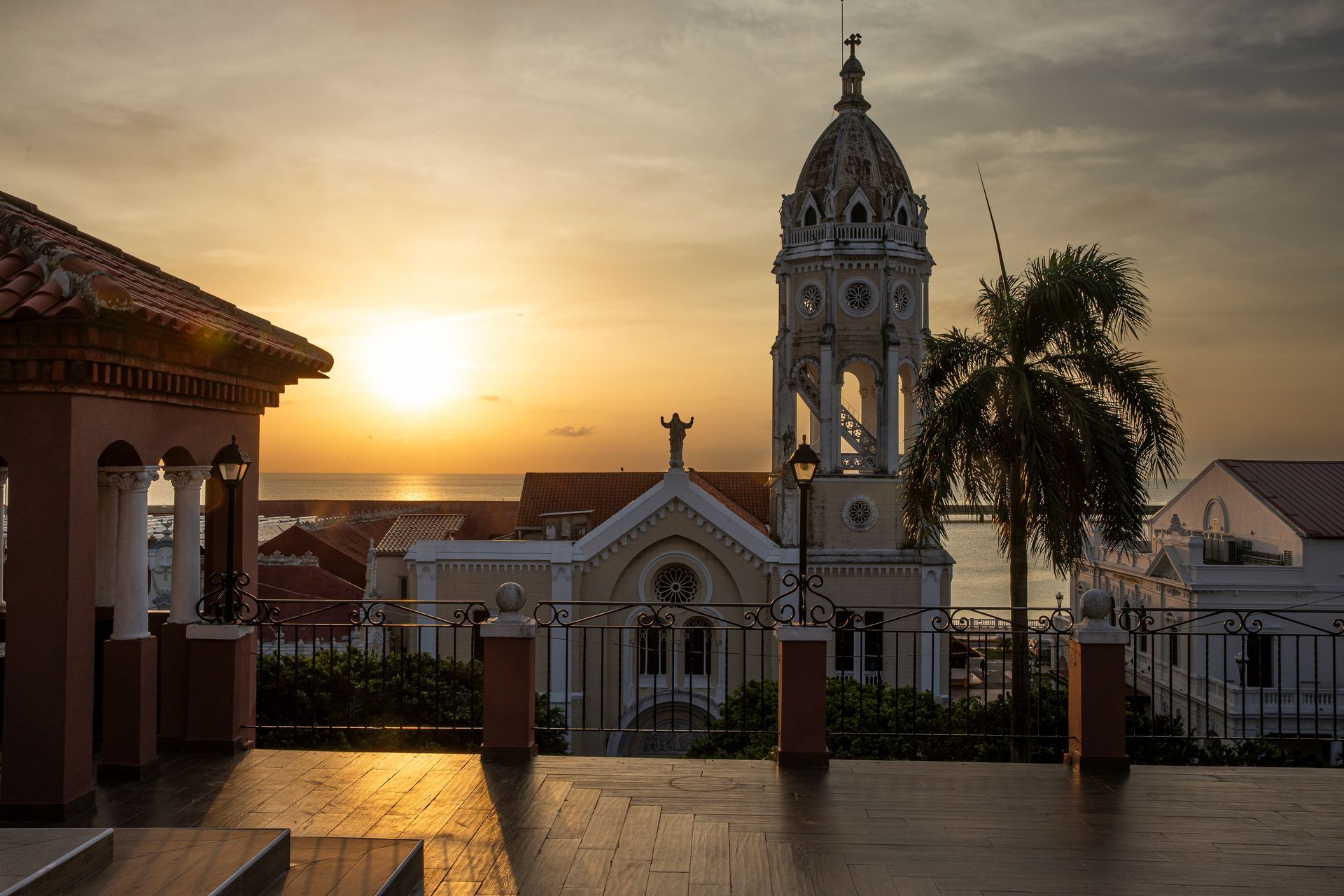 View from PH Hotel Colombia toward San Francisco de Asís Church in Casco Viejo, with golden sunlight, a palm tree, and a tiled terrace in the foreground.