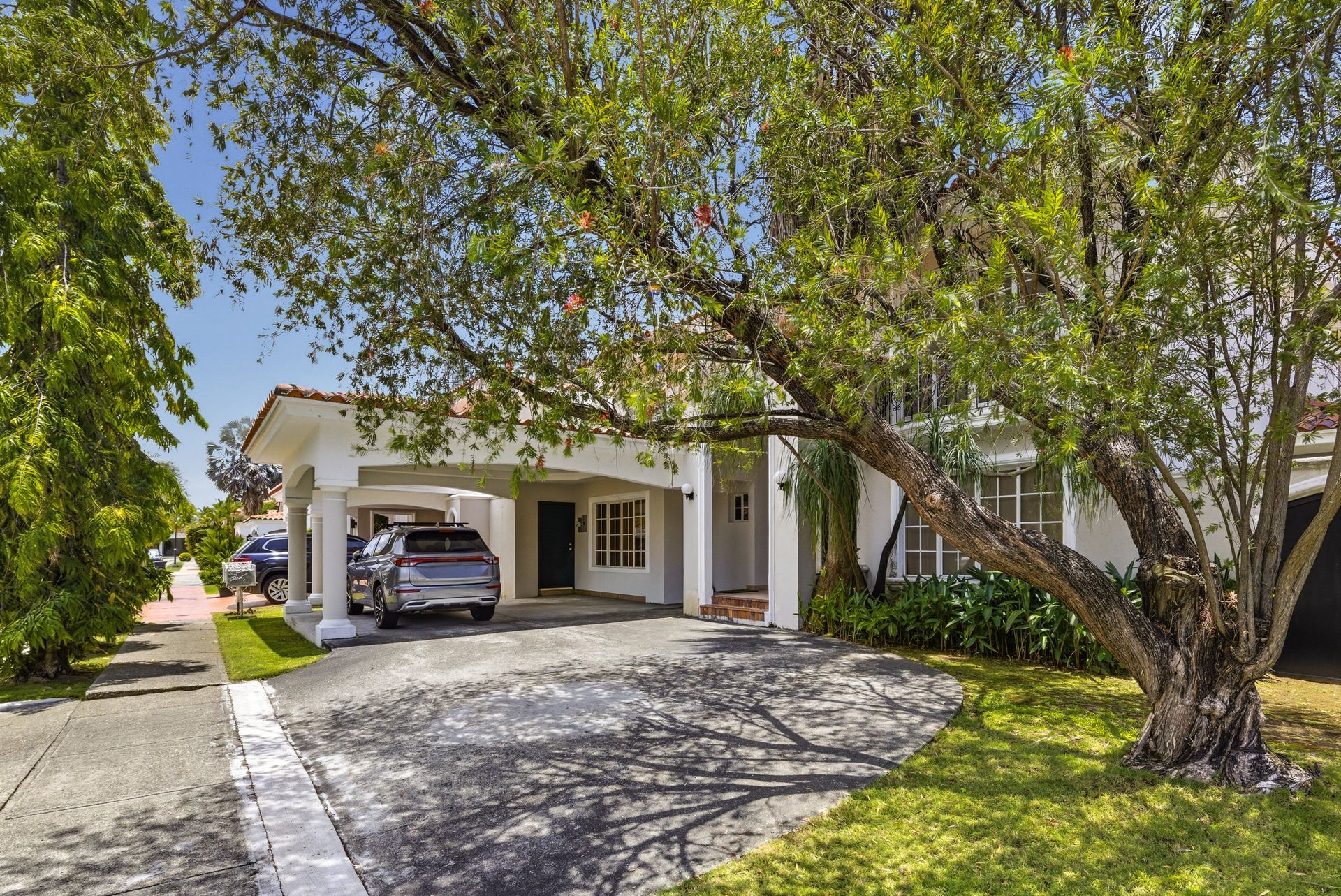 Costa del este panama 
 by Suburban house with car in driveway, surrounded by trees and lawn
