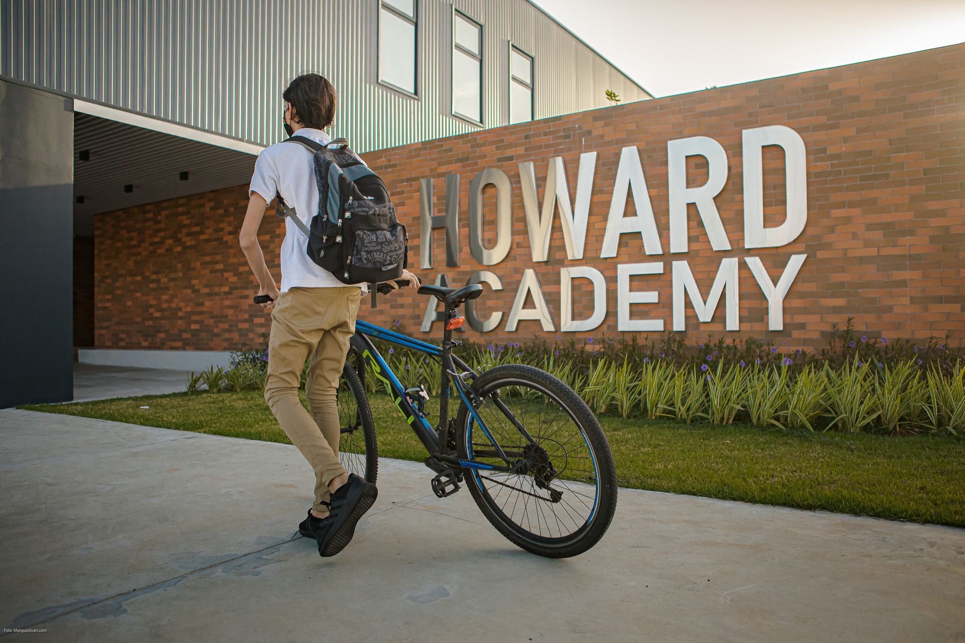 Student with a bicycle in front of the modern Howard Academy brick sign in Panama Pacifico.