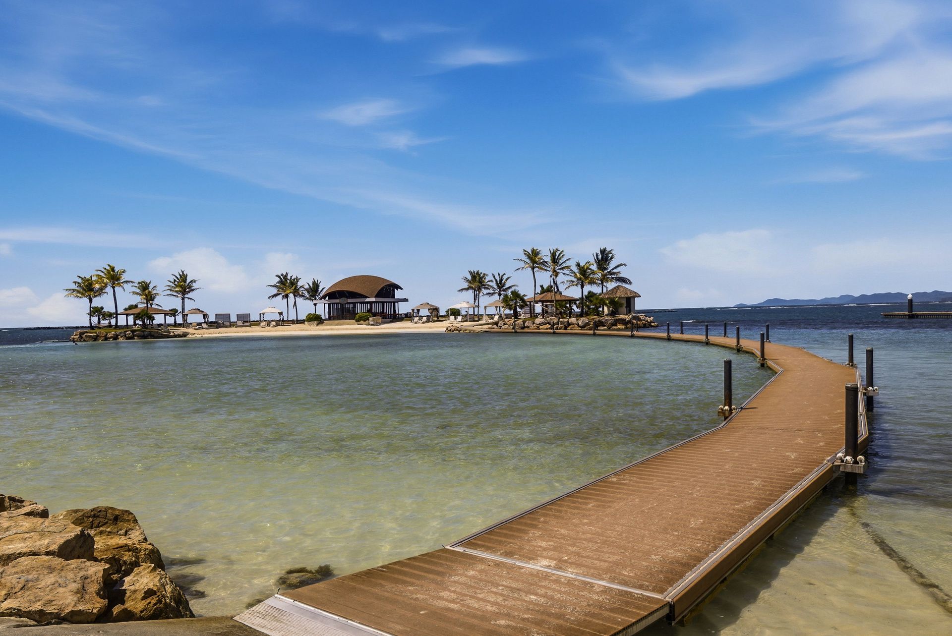Wooden boardwalk over turquoise water connecting the beach to the private restaurant island at Playa Escondida Resort, 
