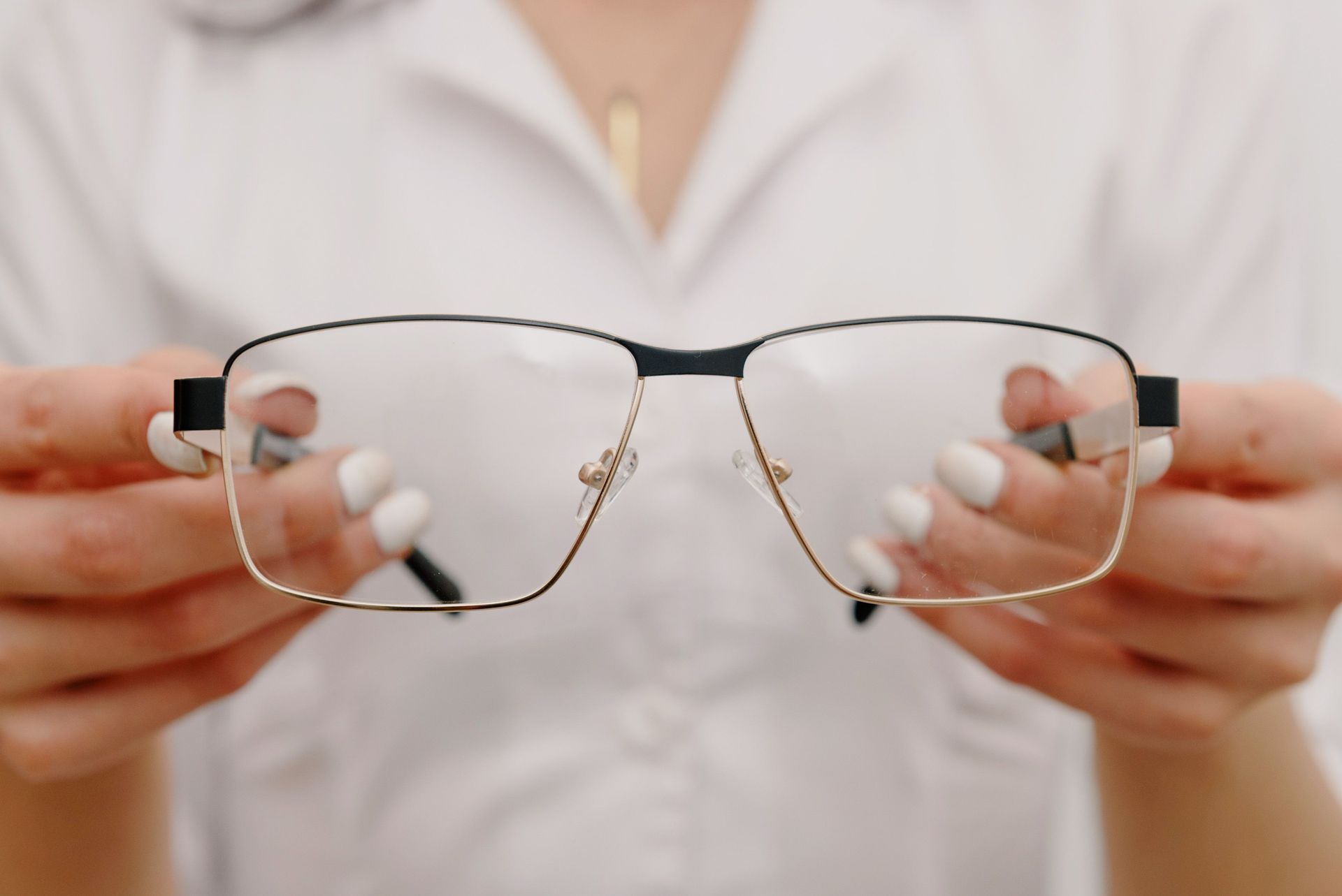 Hands holding frameless eyeglasses in a white shirt background