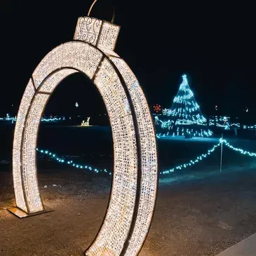 A horseshoe shaped christmas ornament is lit up at night in front of a christmas tree.
