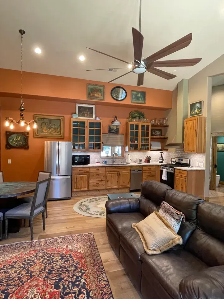 A living room with a couch and a kitchen with a ceiling fan.
