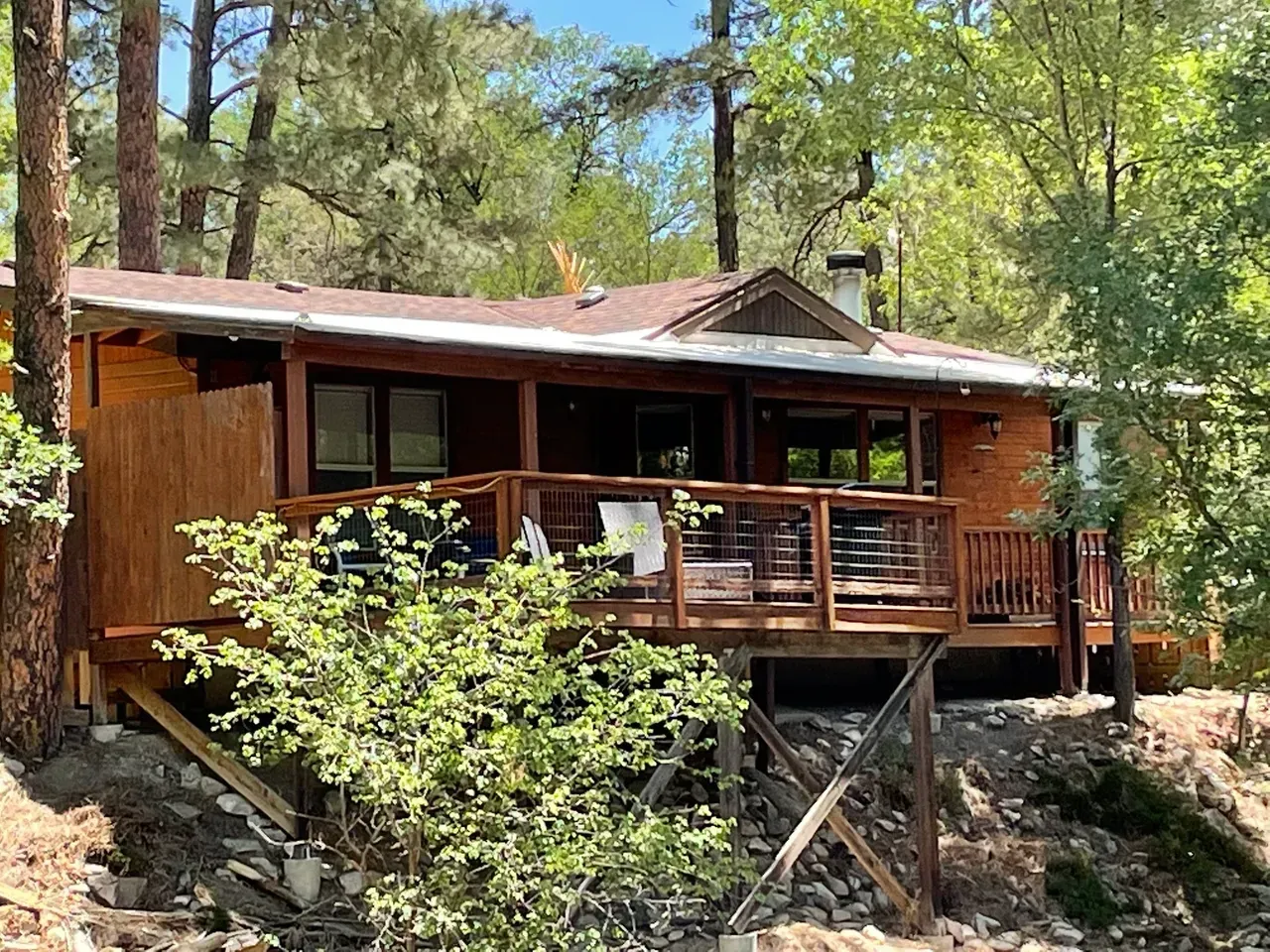 A small wooden house with a large deck in the middle of a forest.