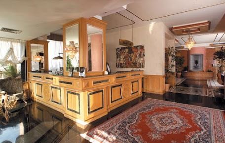 Bancone della reception dell'hotel con bancone in legno, specchio e tappeto rosso a fantasia.