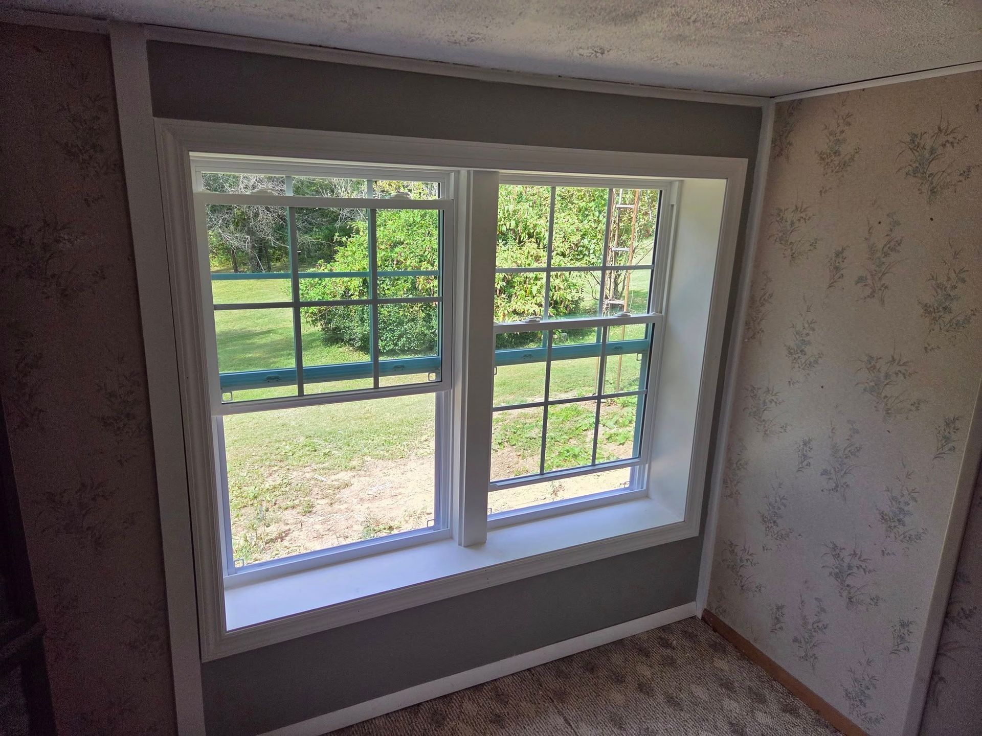 White-framed window in a small room, looking out onto a green yard and fence.