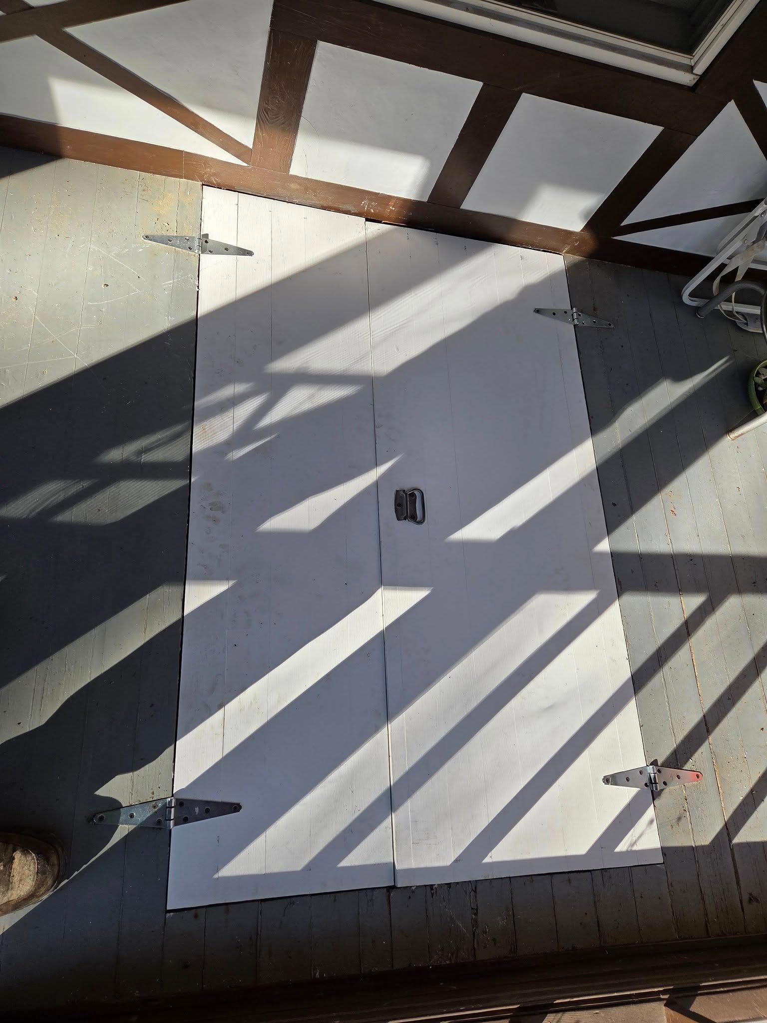 White electrical panel door on a sunlit wall with diagonal shadows from nearby beams.