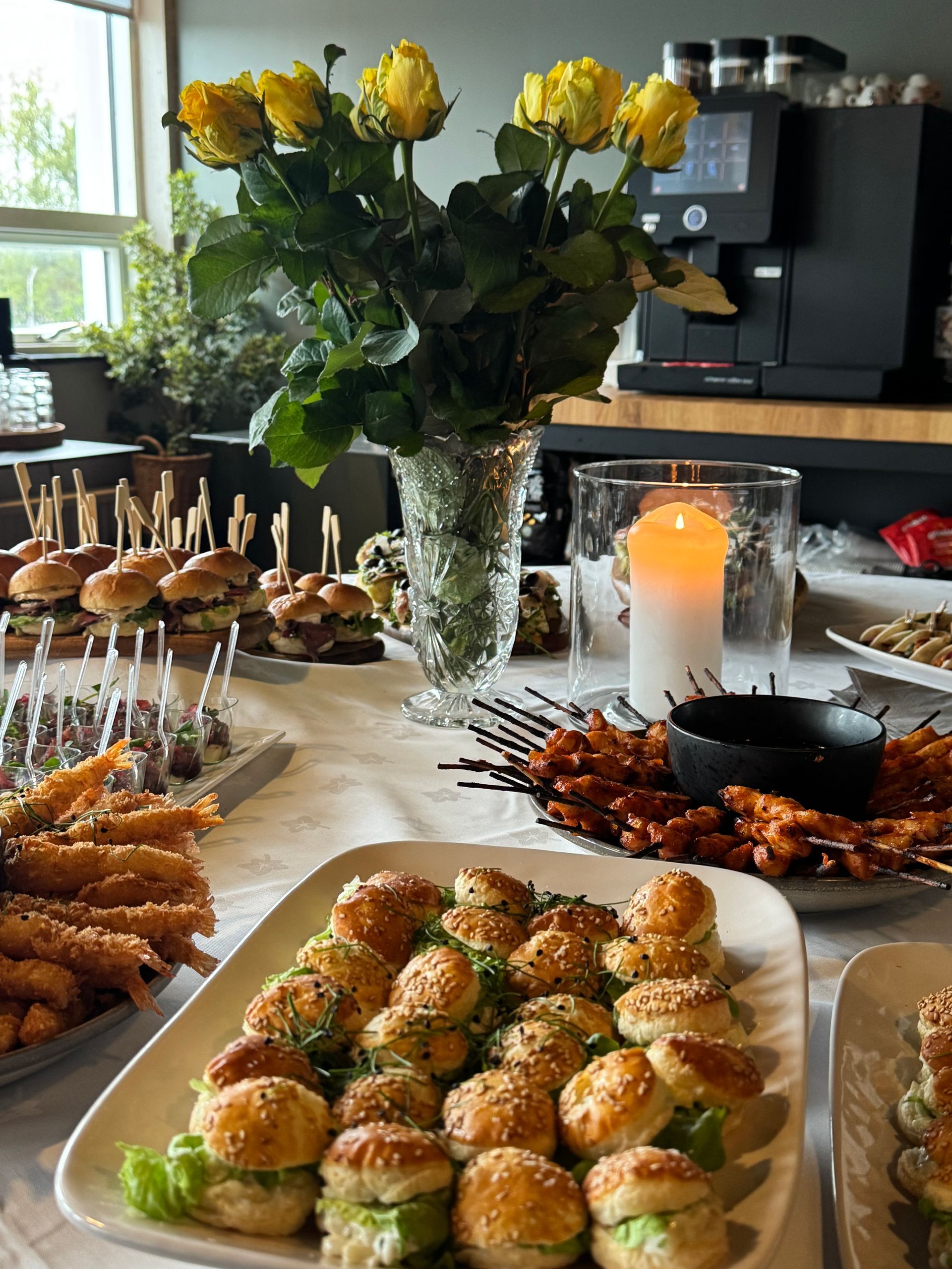 Buffet table with appetizers, candles, and a vase of yellow flowers in a cozy indoor setting