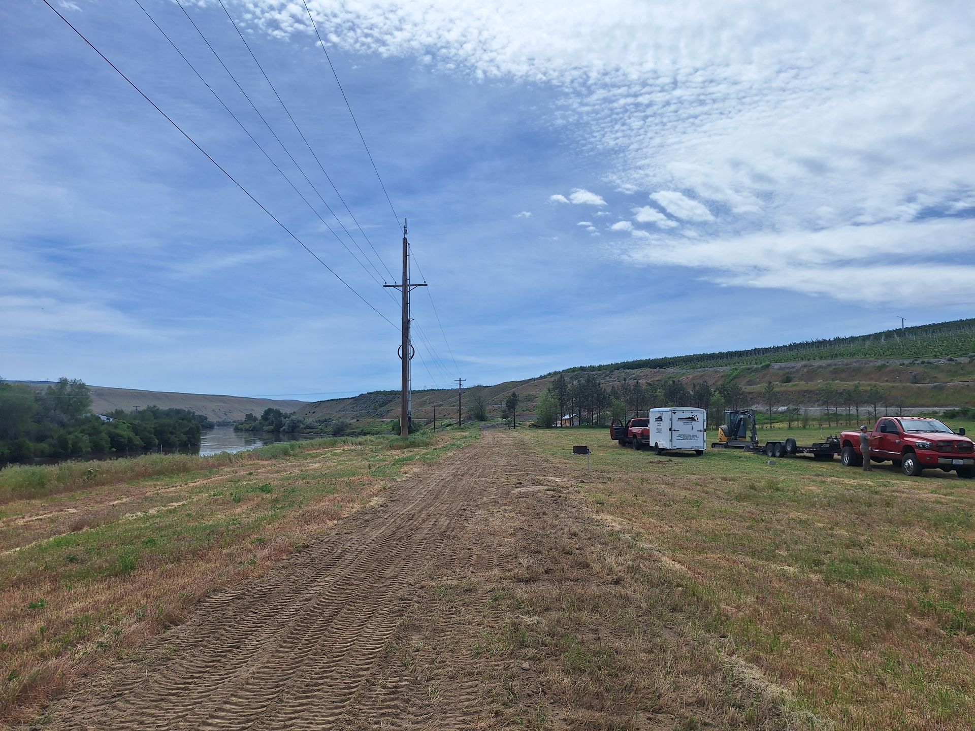 Dirt path leading to power lines under a blue sky, two trucks parked on the side.