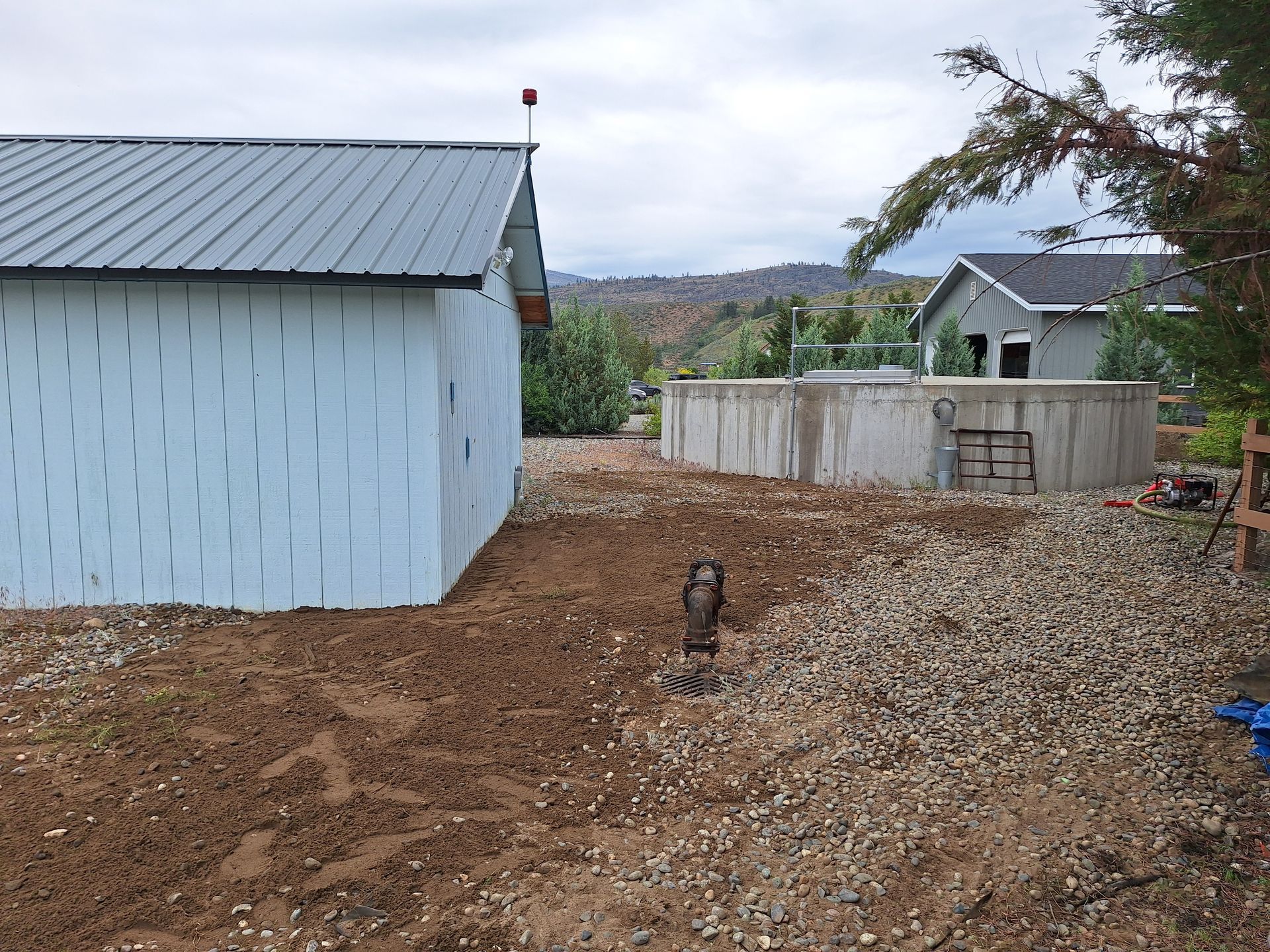 Exterior view of a light blue building and concrete circular structure. Gravel ground, cloudy sky.