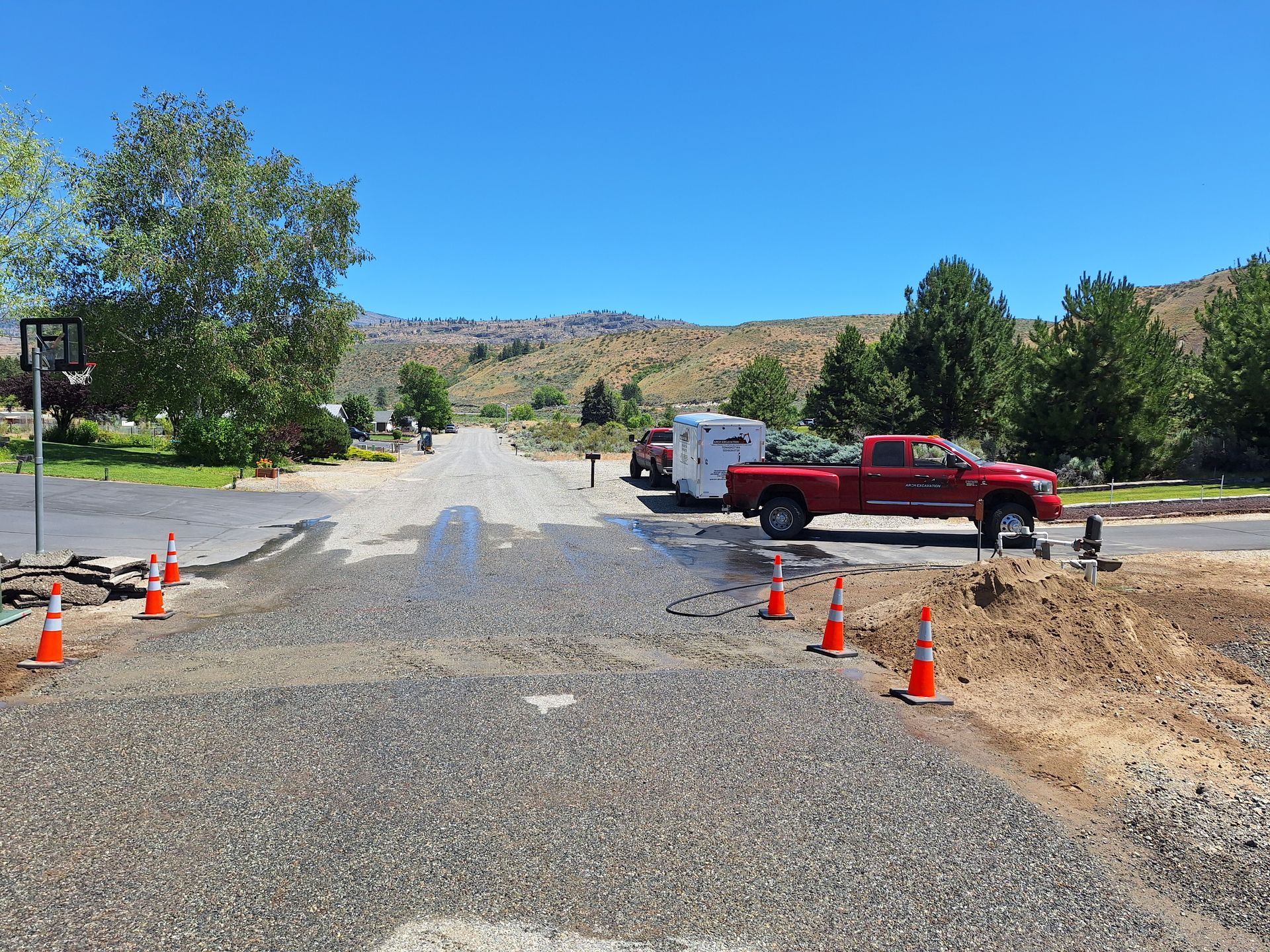 Road construction site with red truck, trailer, and orange traffic cones under a blue sky.