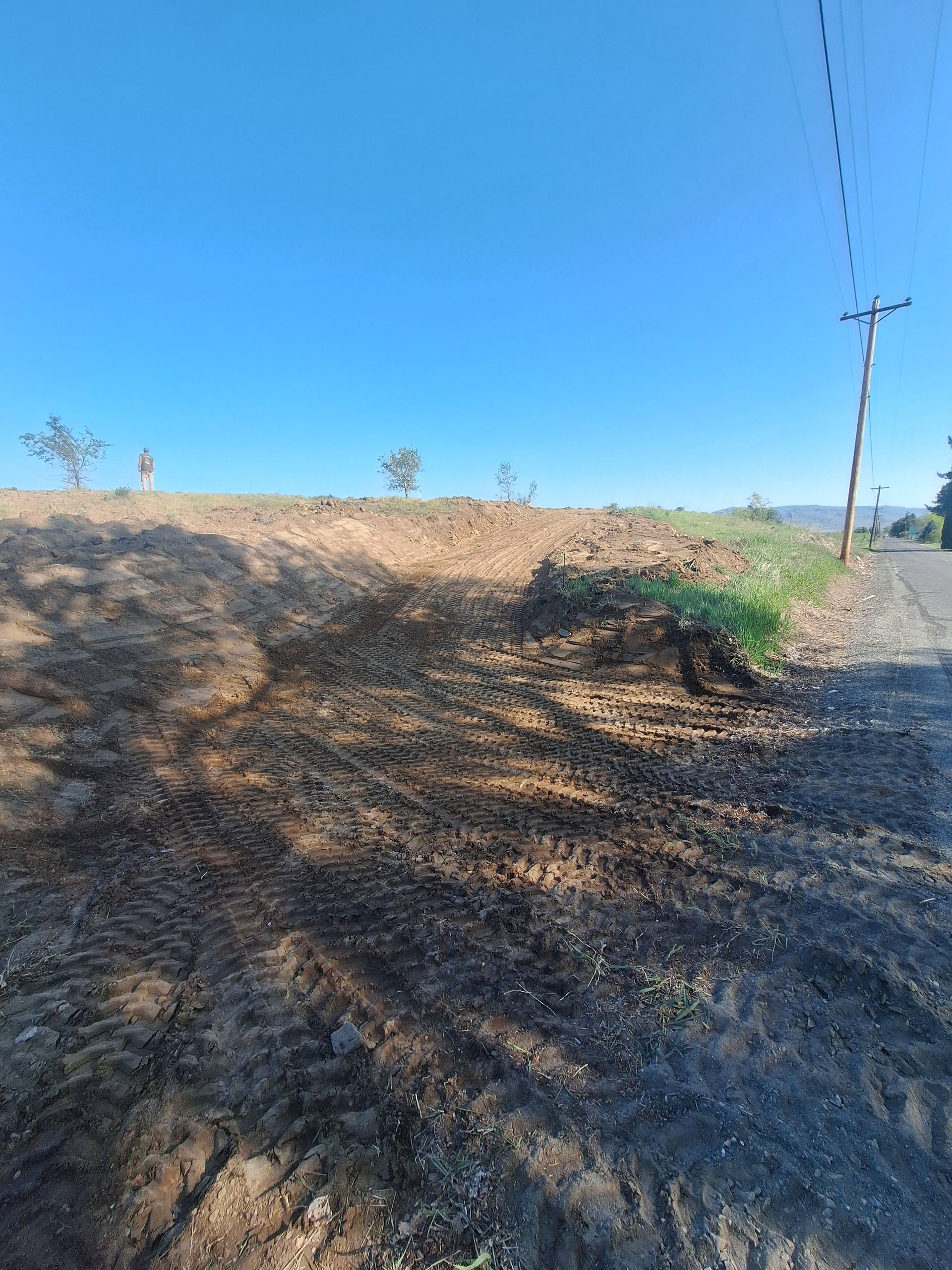 Dirt road leading to a cleared, elevated lot with sparse vegetation under a blue sky.