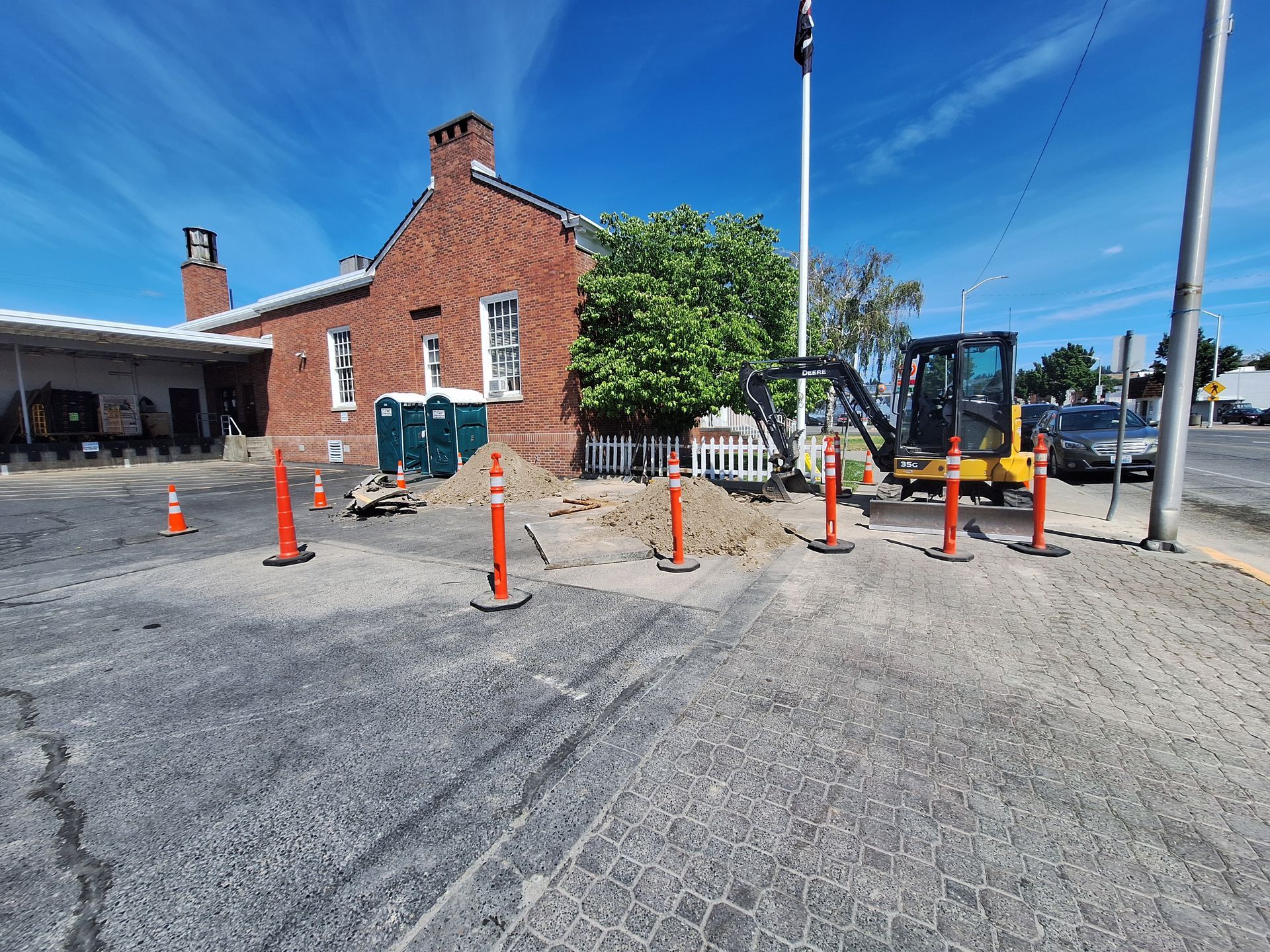 Construction site with an excavator next to a brick building. Orange cones mark off area.