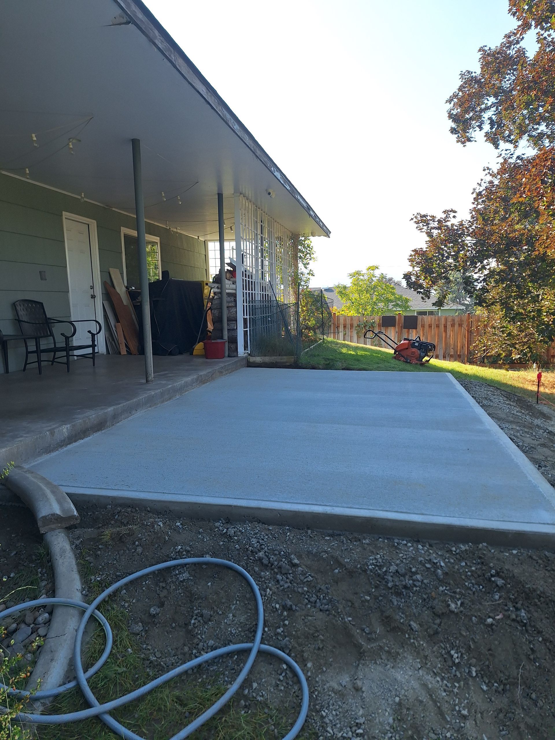 Newly poured concrete patio next to a house with a covered porch. Grey, sunny, outdoor.
