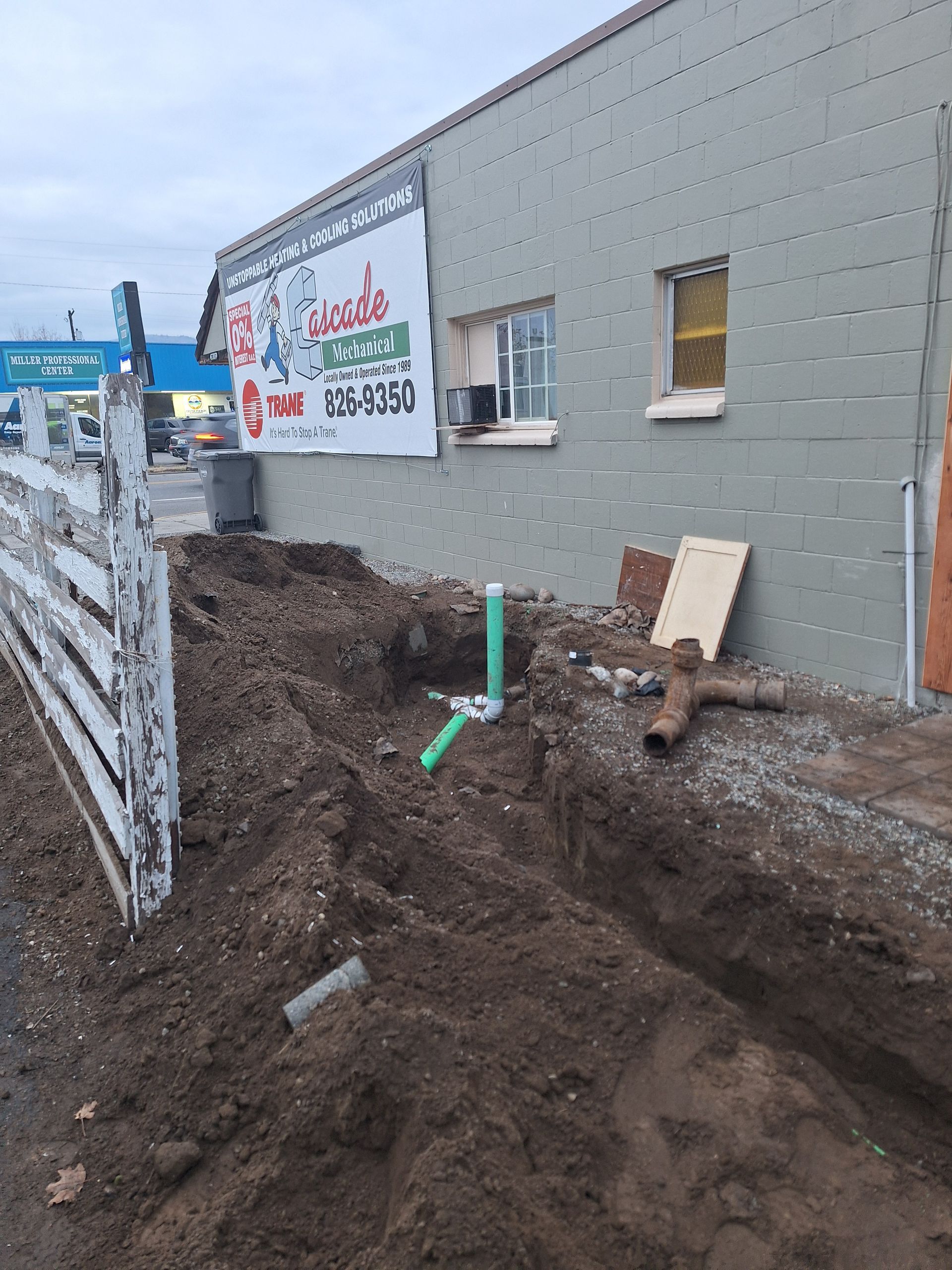 Exterior view of construction site. Trench dug near building with exposed pipes and soil.