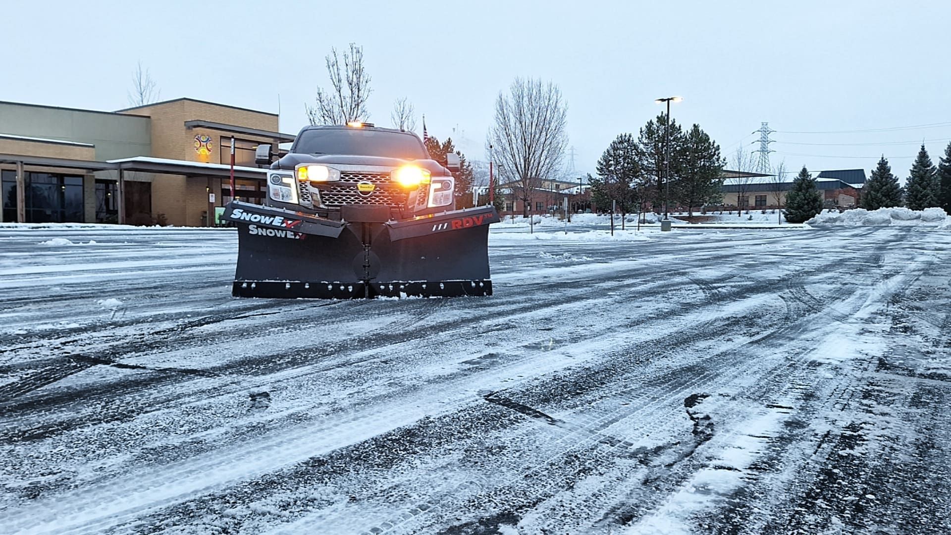 Snowplow clearing a snow-covered parking lot on a cloudy day.