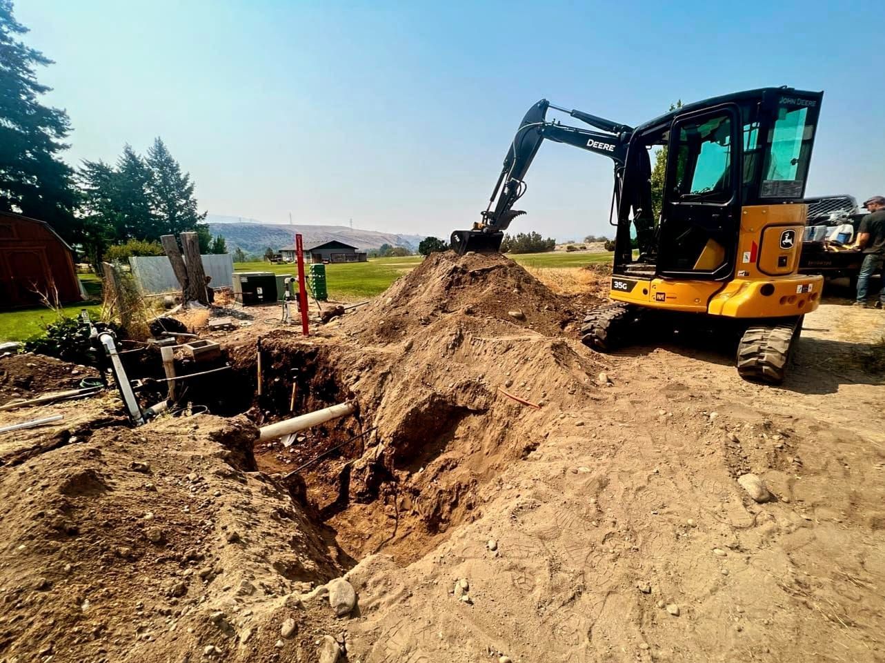 Yellow excavator digging in a dirt pit outdoors under a blue sky.
