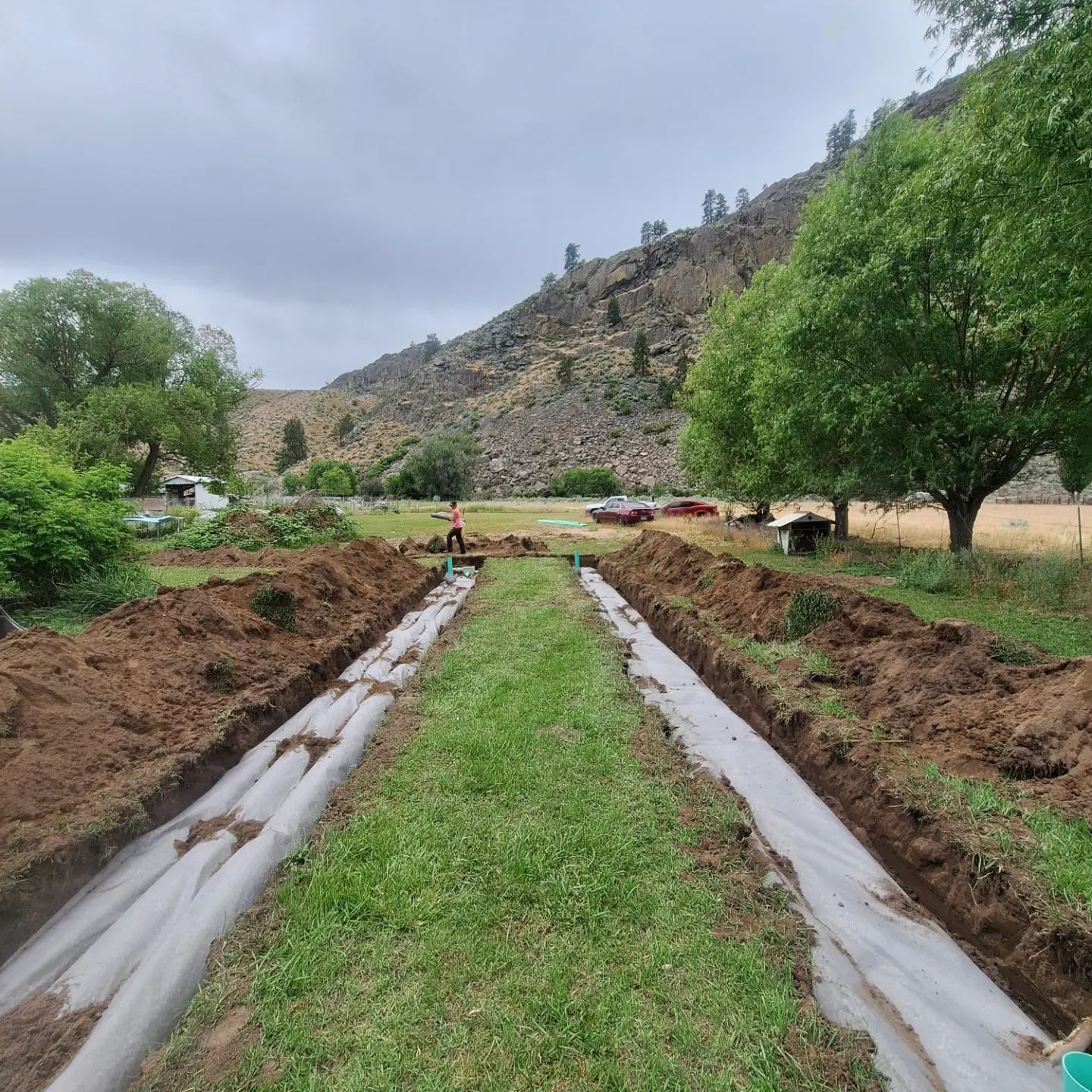 Two long trenches with fabric, grass center, mountain backdrop.