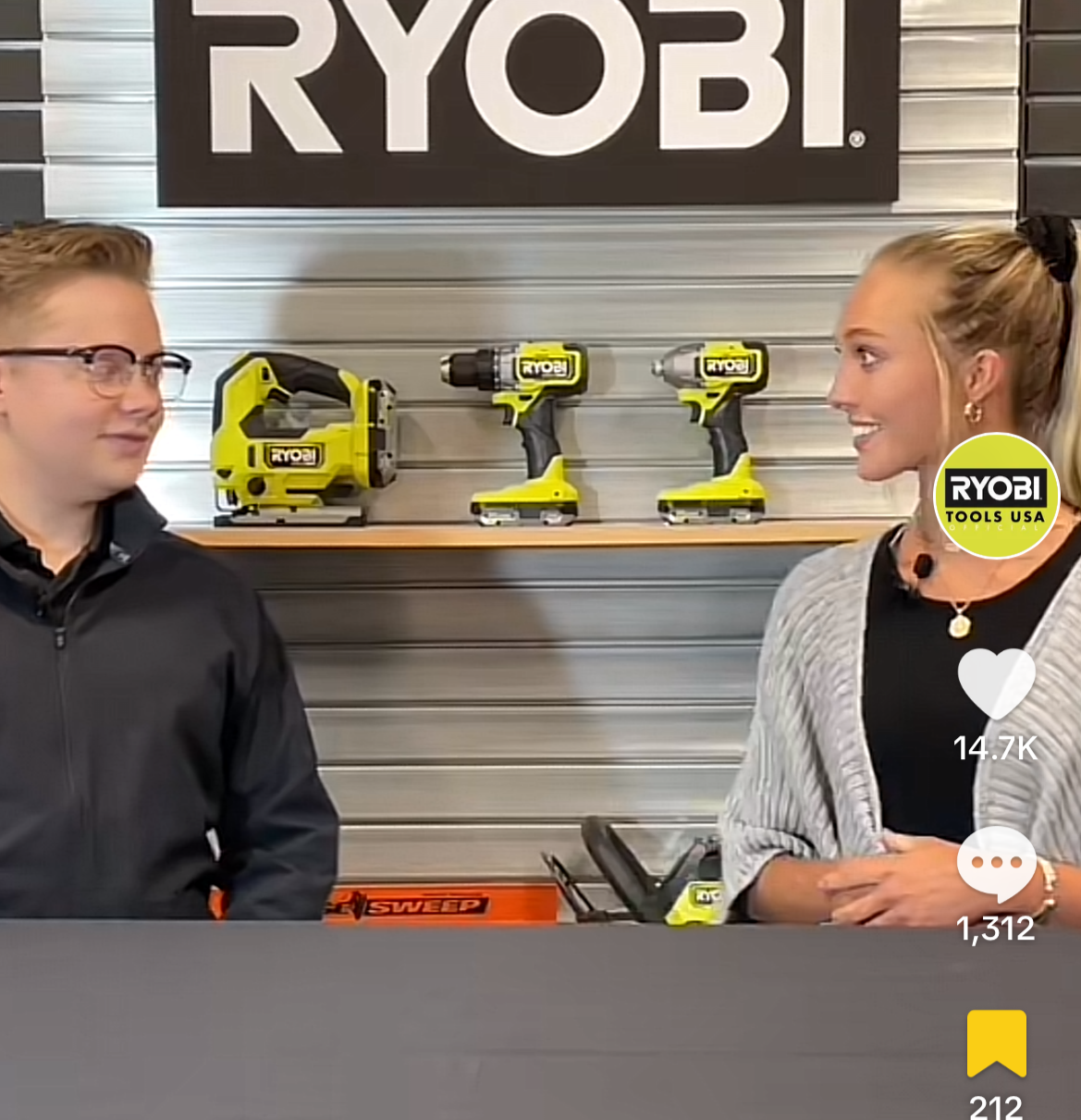 Two people talking in a Ryobi tool display area, with yellow power tools on shelves behind them.