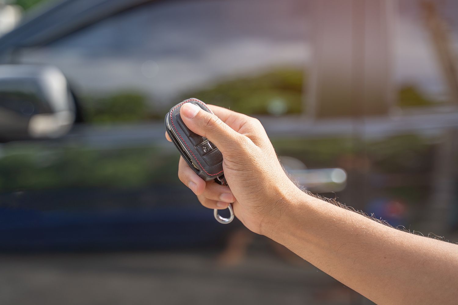 A person is holding a remote control in their hand in front of a car.