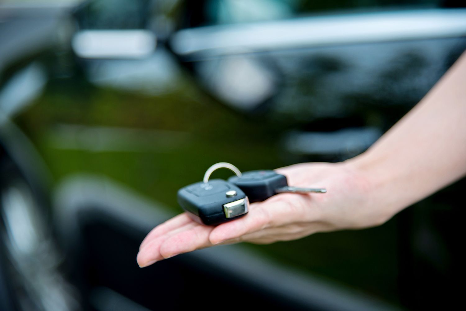 A person is holding a pair of car keys in front of a car.