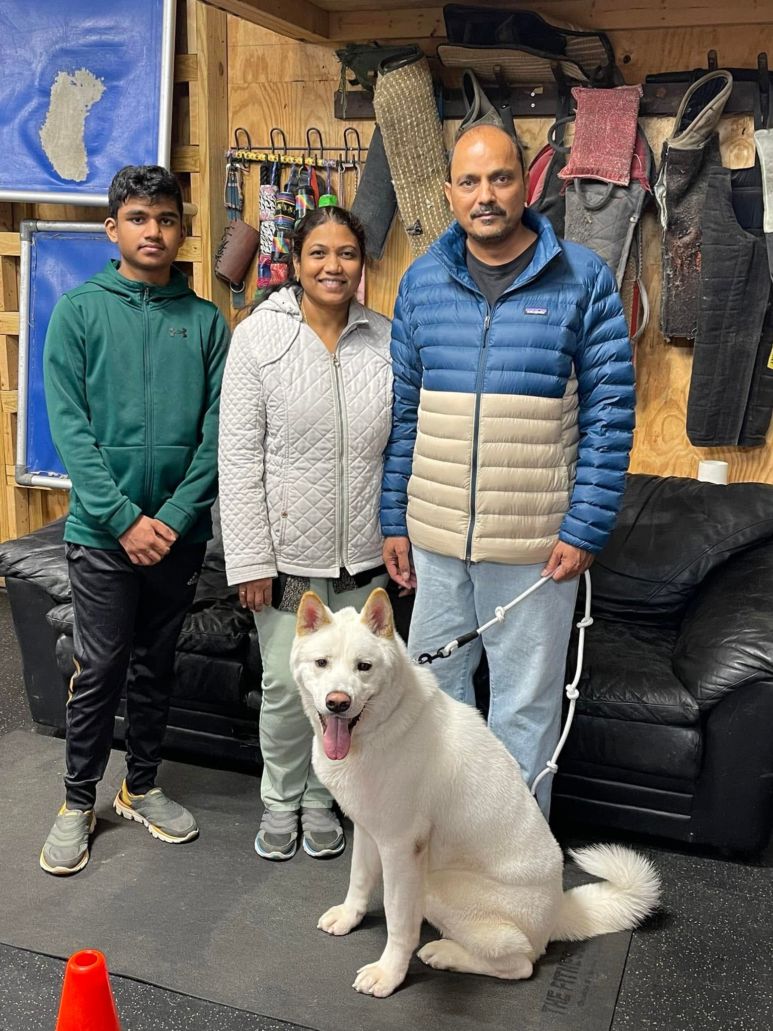 Three people standing indoors with a white dog sitting in front of them