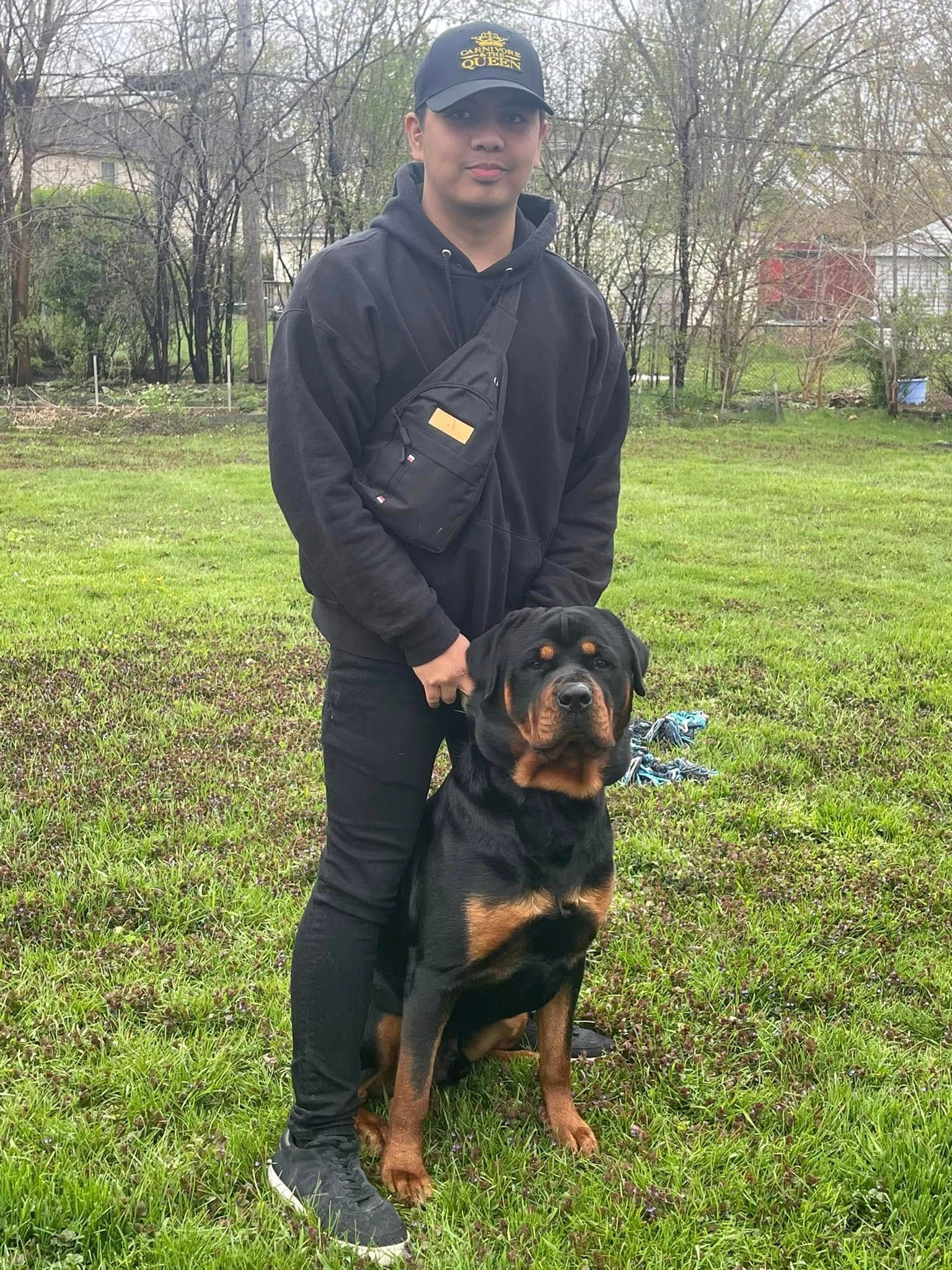 Person standing with a Rottweiler in a grassy park, both facing the camera.