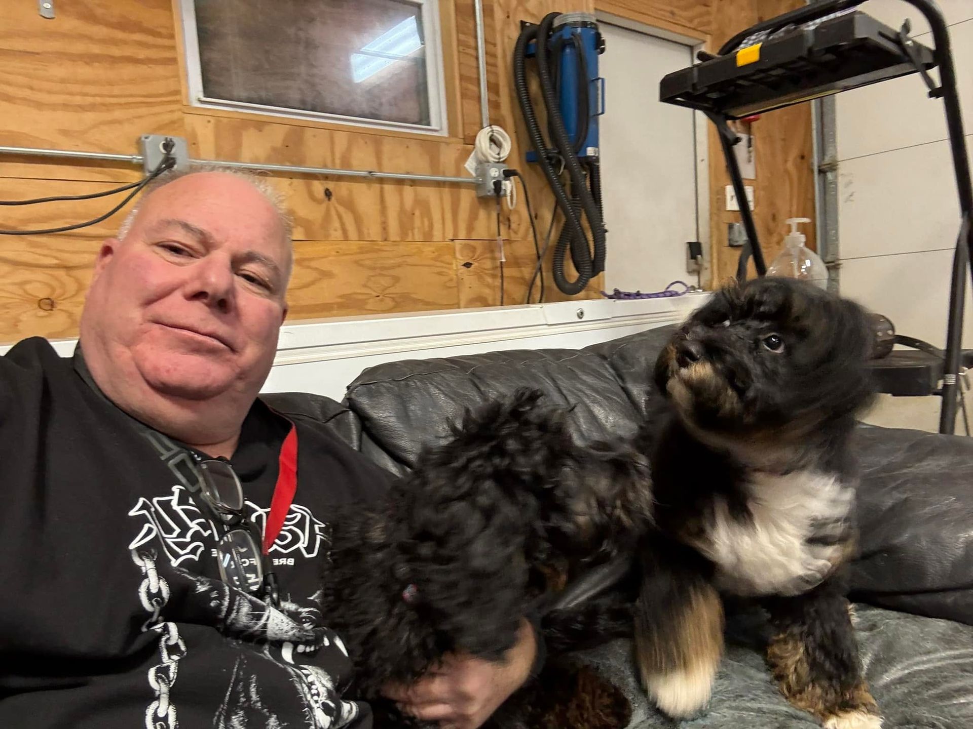 Man smiling on a couch with two fluffy dogs in a wood-paneled room