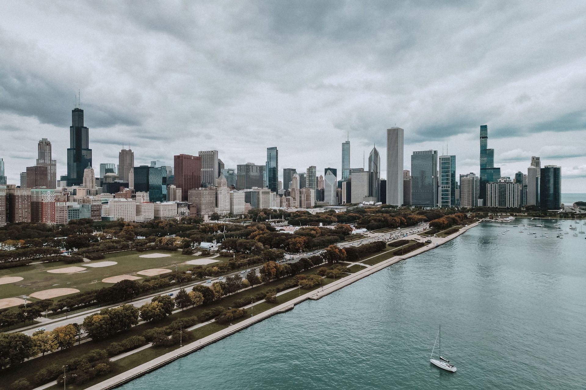 Chicago skyline along Lake Michigan under cloudy skies, with a shoreline path and a small boat on the water