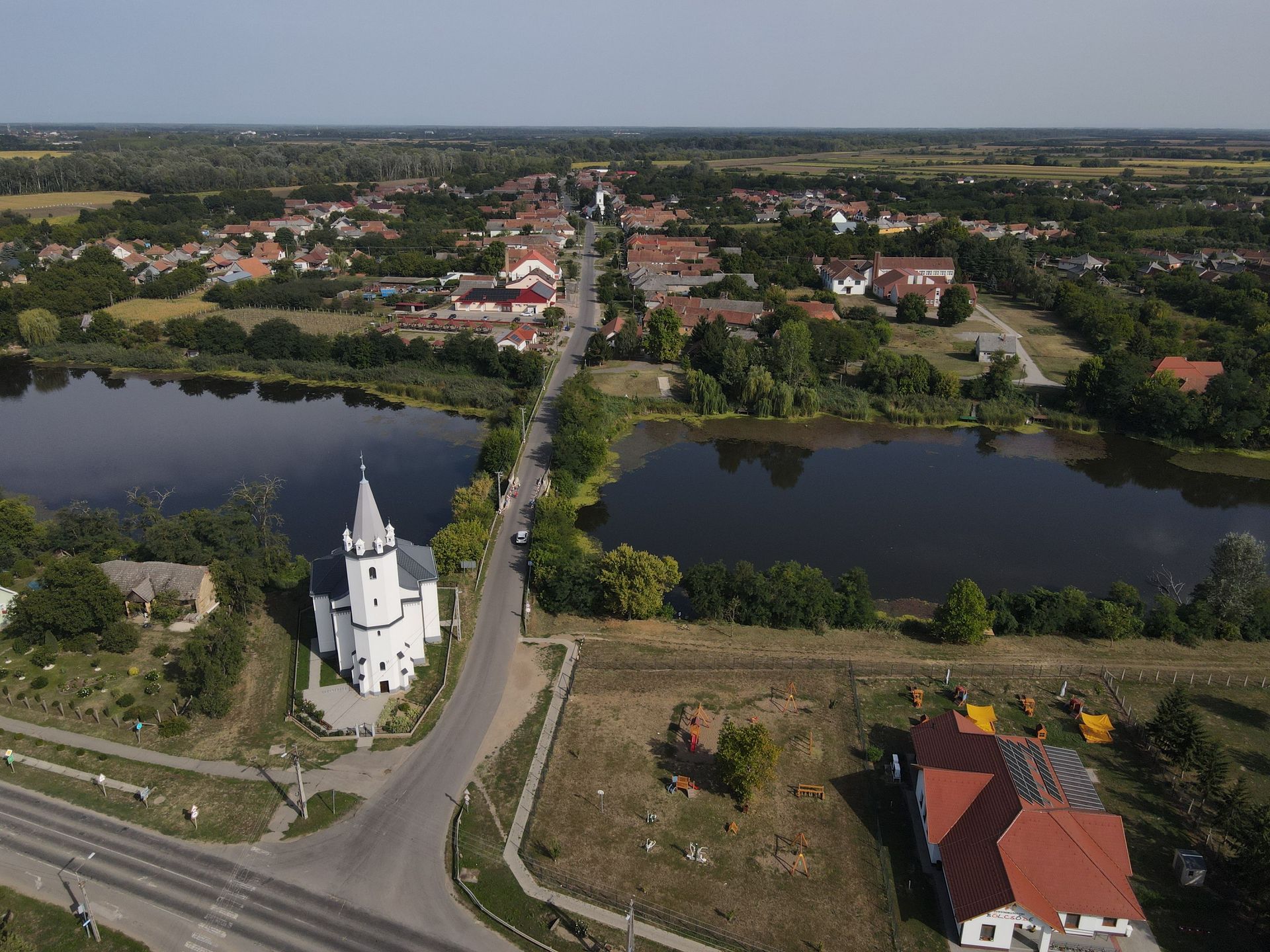 Aerial view of a town with a church, road, and two lakes surrounded by houses and trees.