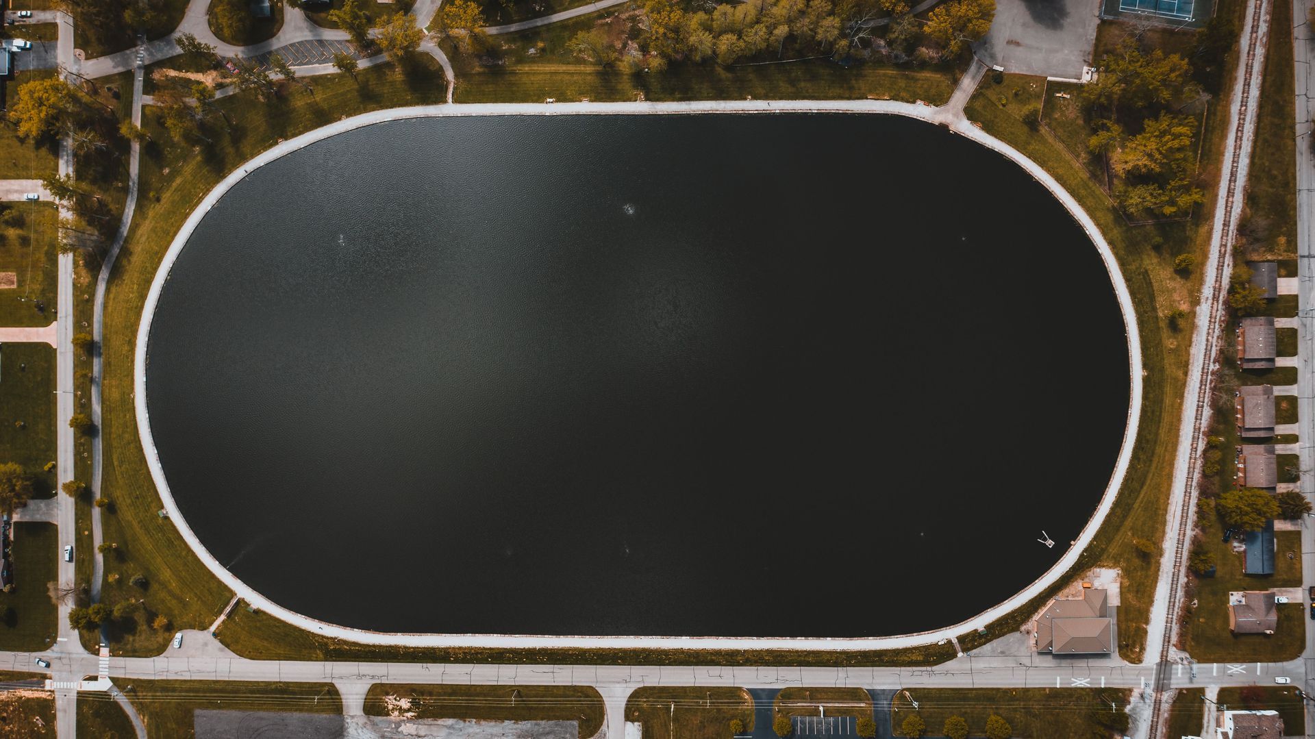 Aerial view of an oval dark water reservoir surrounded by roads and trees.