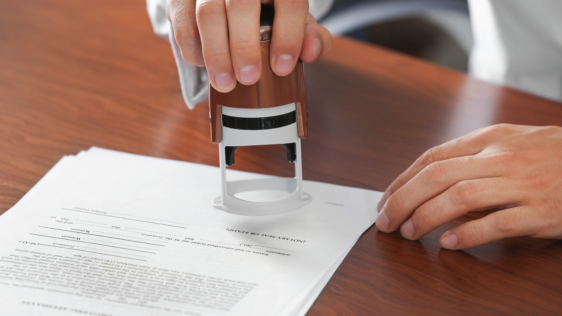 Hands using a stamp on a document at a wooden desk