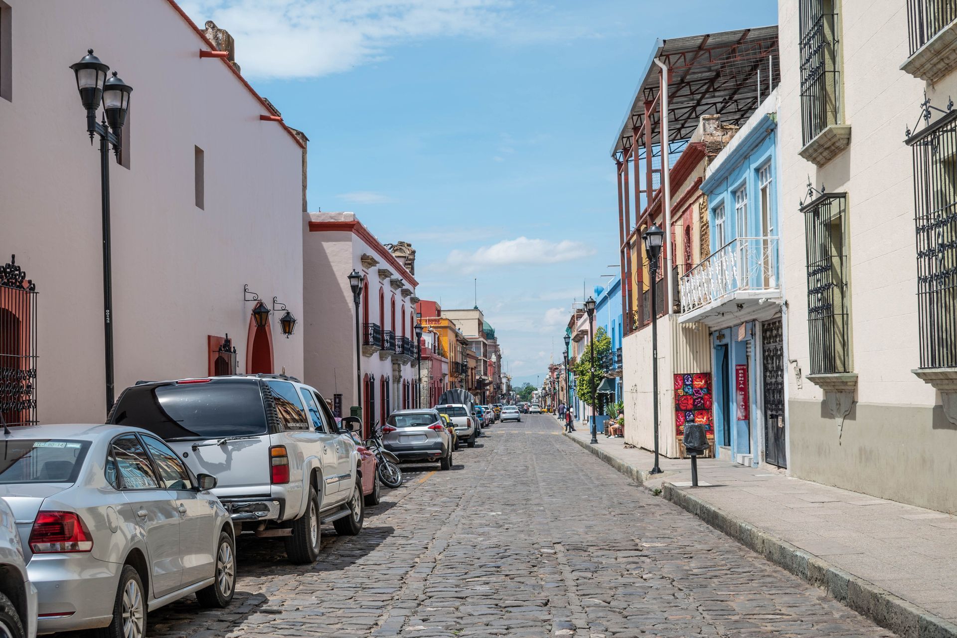 Cobblestone street with parked cars and colorful buildings under a blue sky