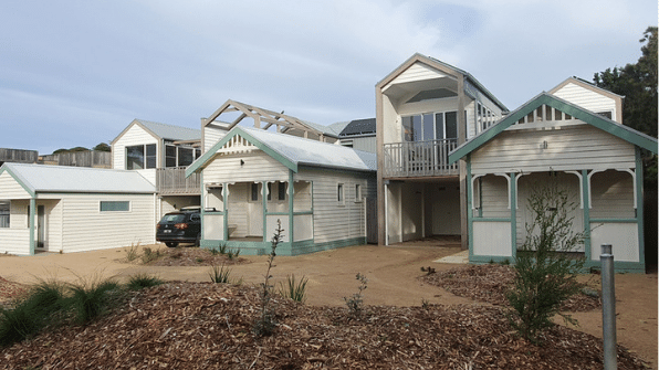 A collection of wooden beach-style cottages with light walls and pale green trim arranged on a sandy, landscaped lot.