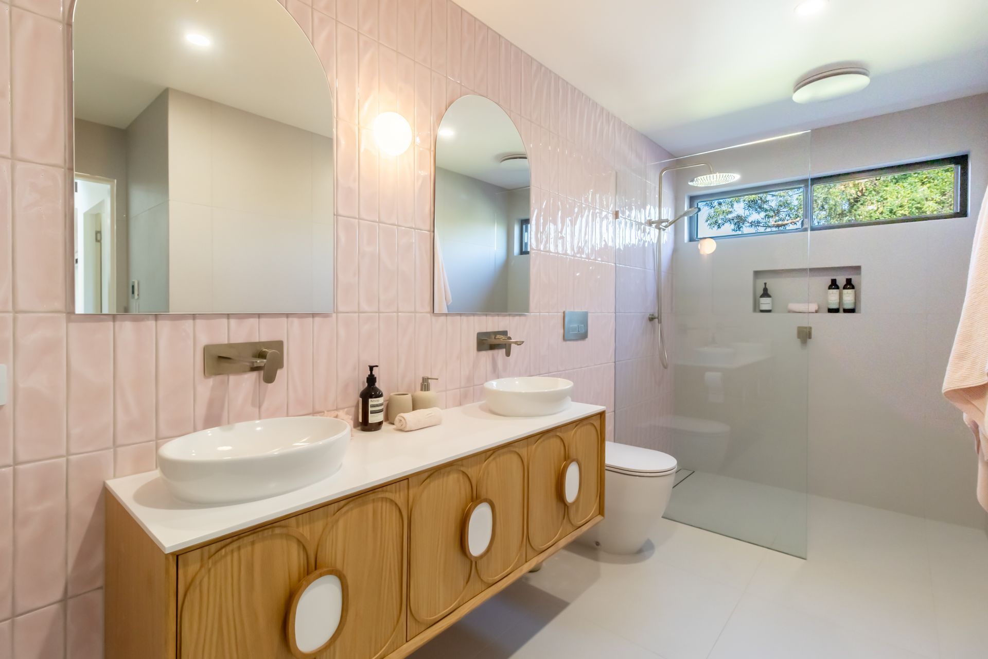 A bathroom with pink tiles , two sinks , a toilet and a walk in shower.