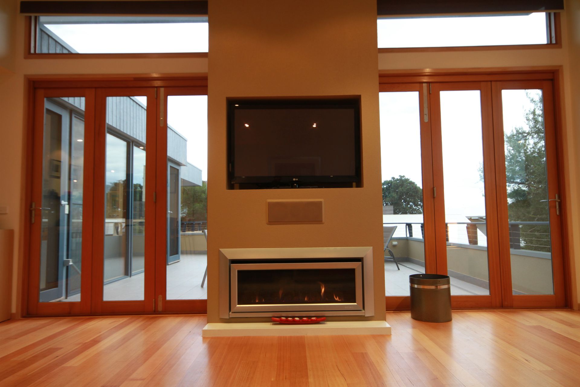 A central fireplace and mounted television on a tan wall, flanked by glass patio doors and hardwood floors.