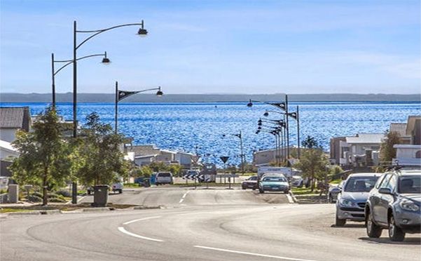 A street with cars parked on the side of it and a view of the ocean.