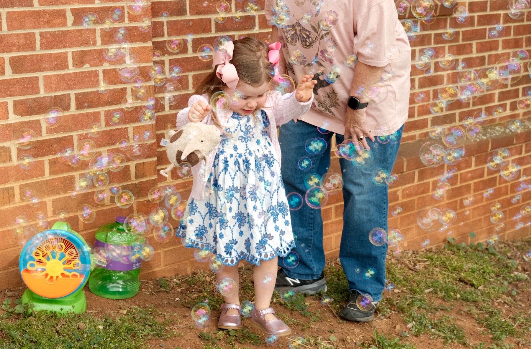 A toddler playing in the bubbles with an adult nearby