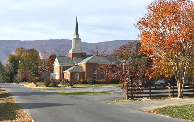 Crozet Baptist Church with steeple beside a road, framed by autumn trees and mountains.