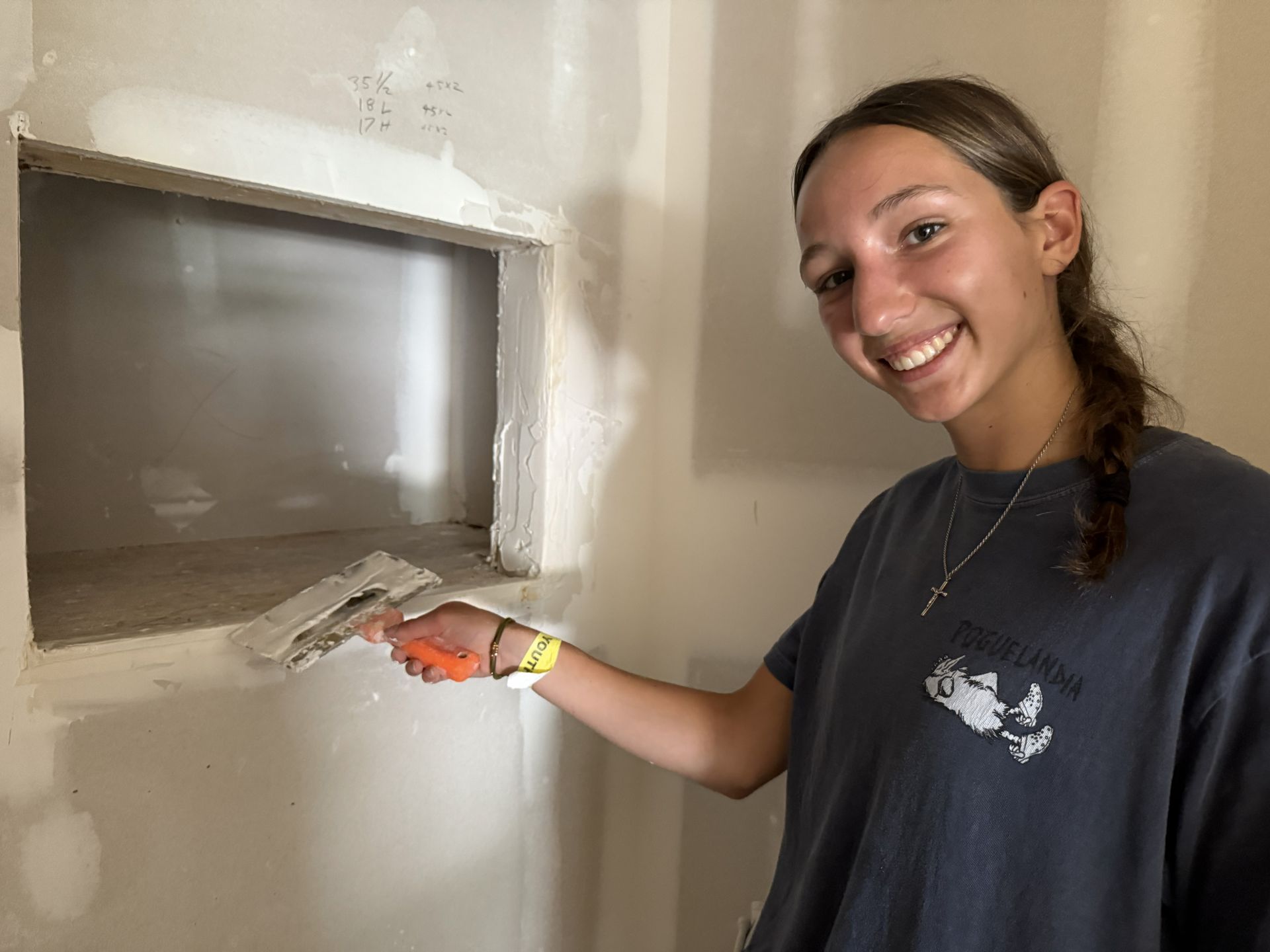 Youth volunteer smiling while applying plaster to a wall niche with a trowel