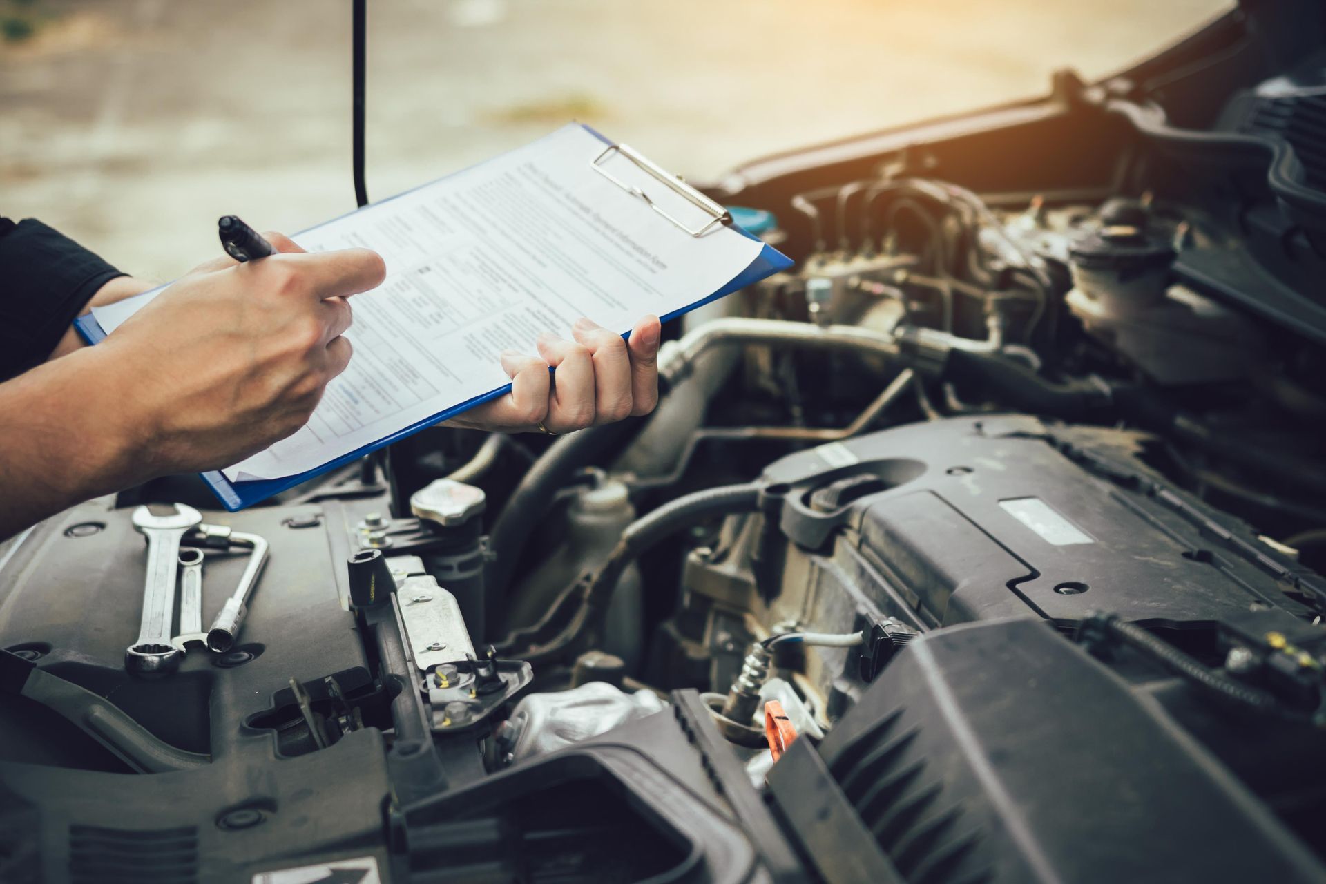 Mechanic with clipboard inspecting a car engine in a garage.