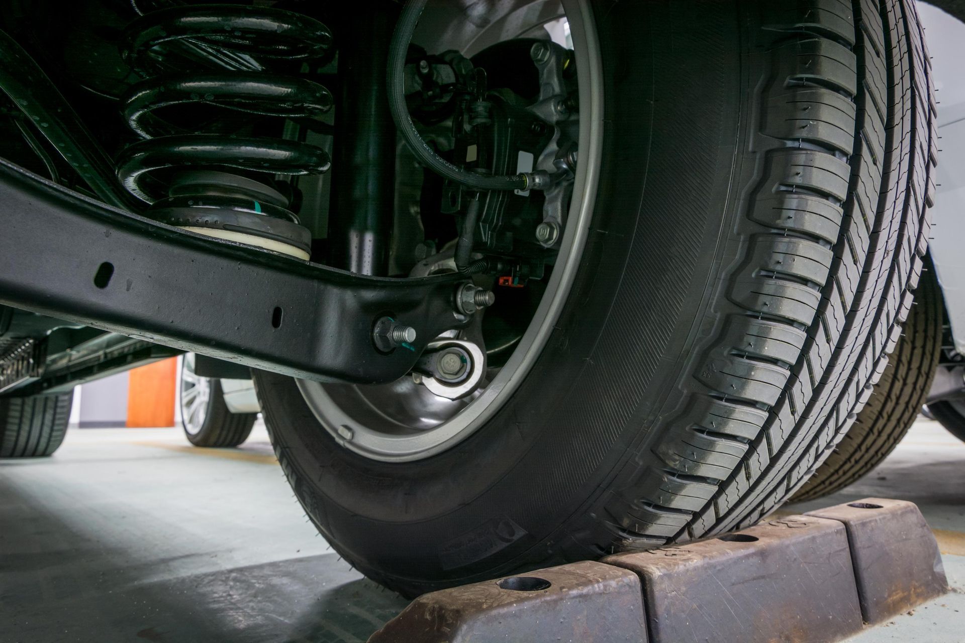 Close-up of a car tire resting on a black parking block; the suspension is visible.