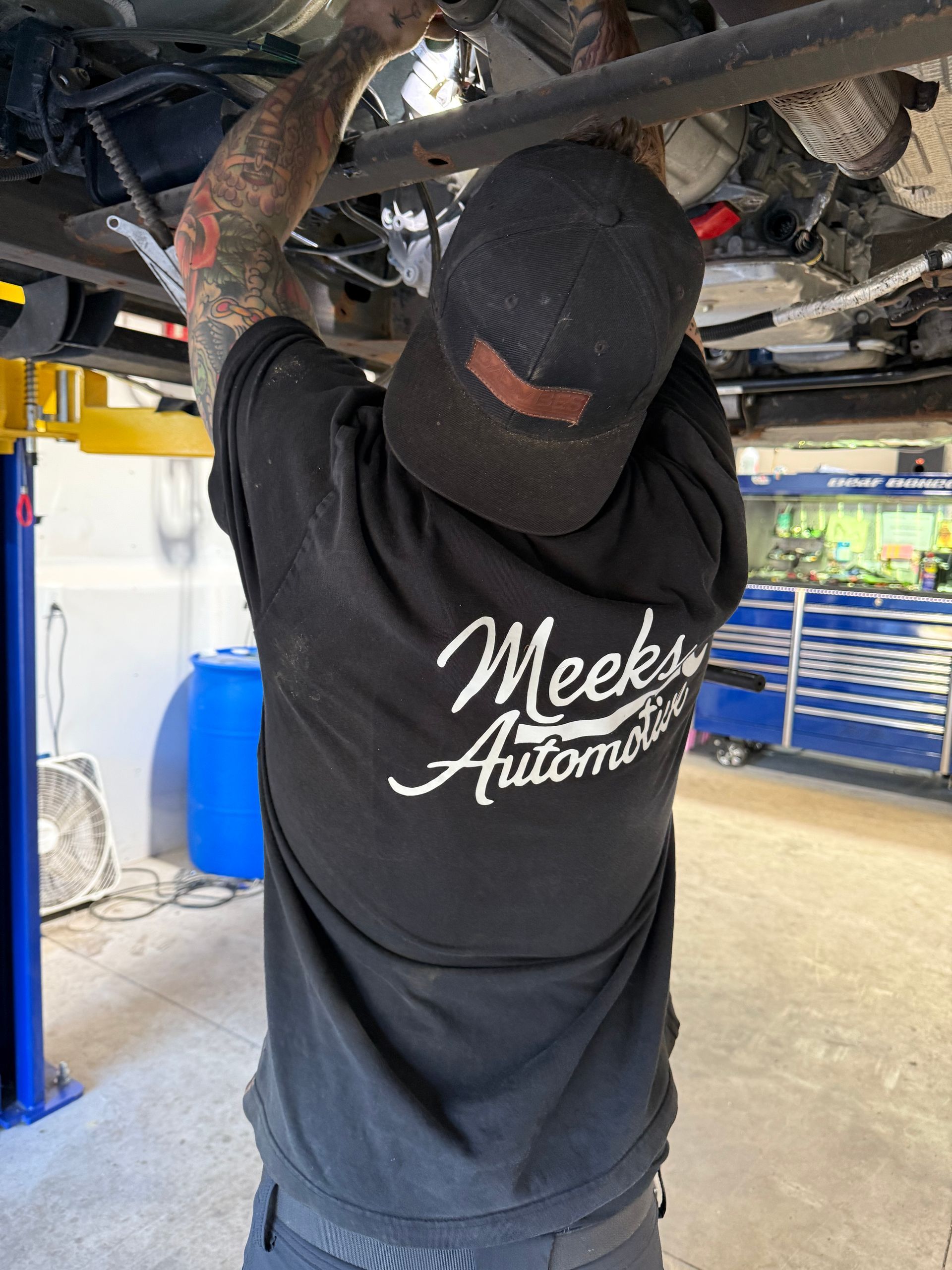 Mechanic inspecting a car's undercarriage with a flashlight in a garage.