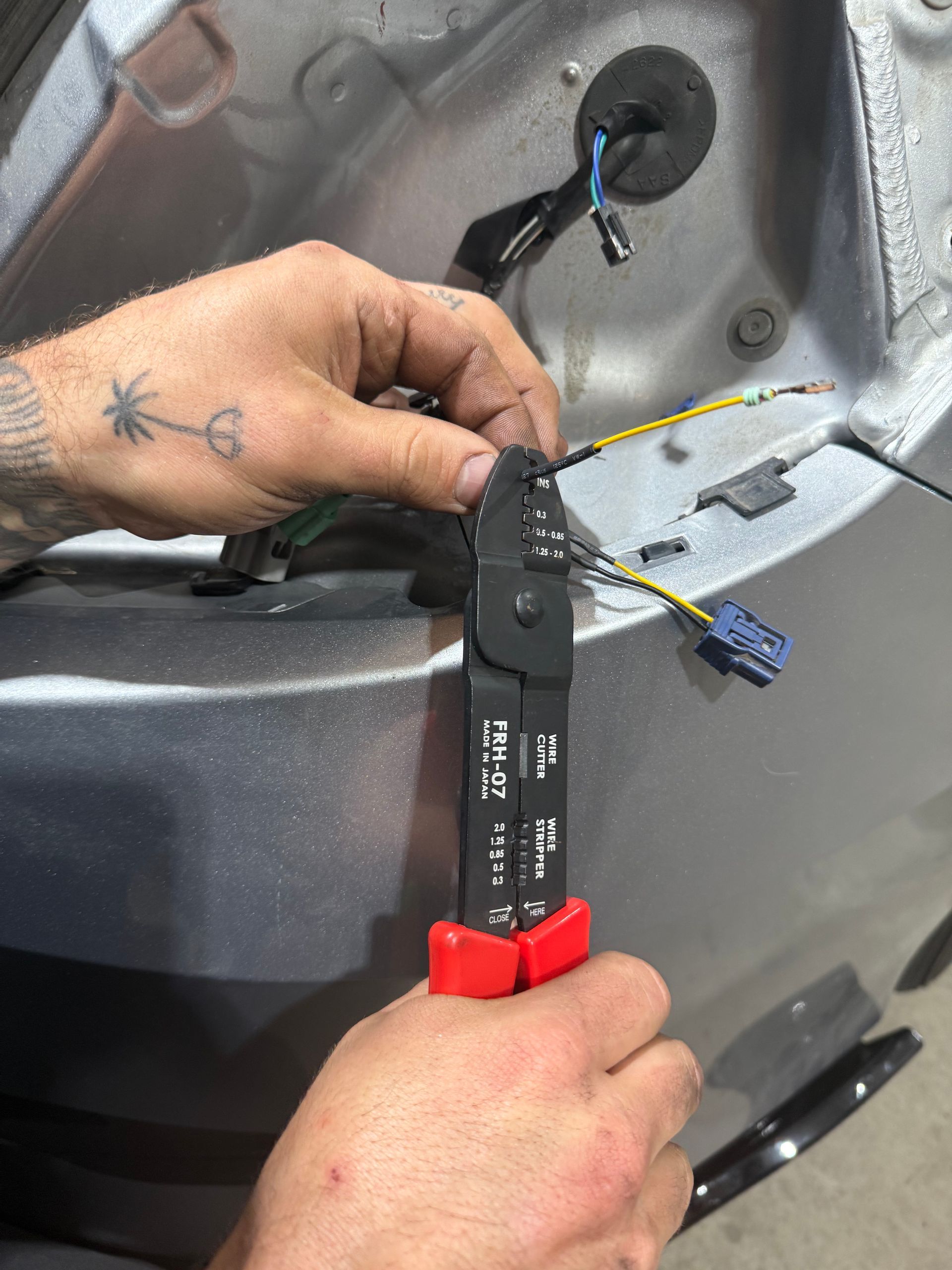 Hands testing a car's engine with a multimeter, laptop nearby. Automotive repair in progress.