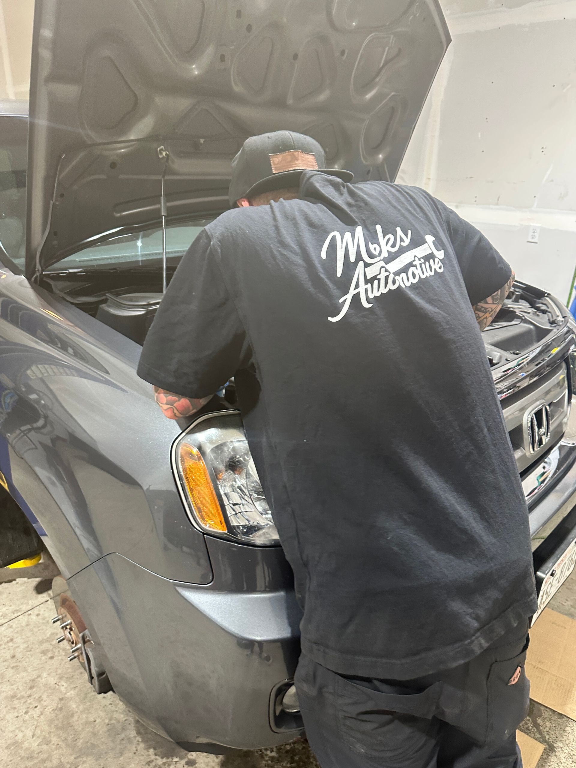 Mechanic using a wrench on a car engine with the hood open; indoor setting.