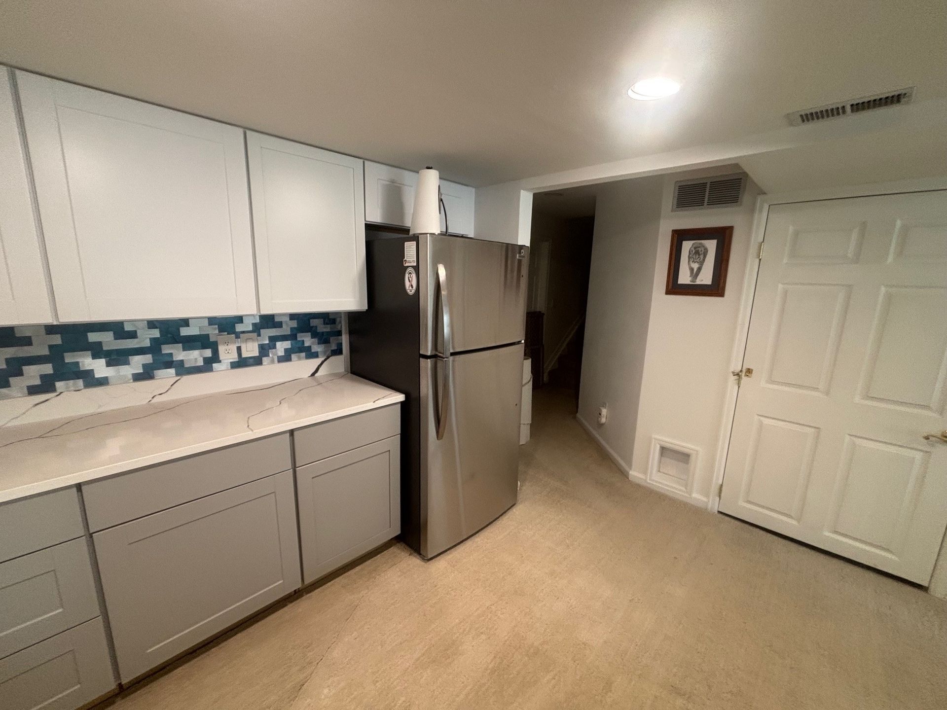 Kitchen with gray and white cabinets, stainless steel fridge, blue tile backsplash.
